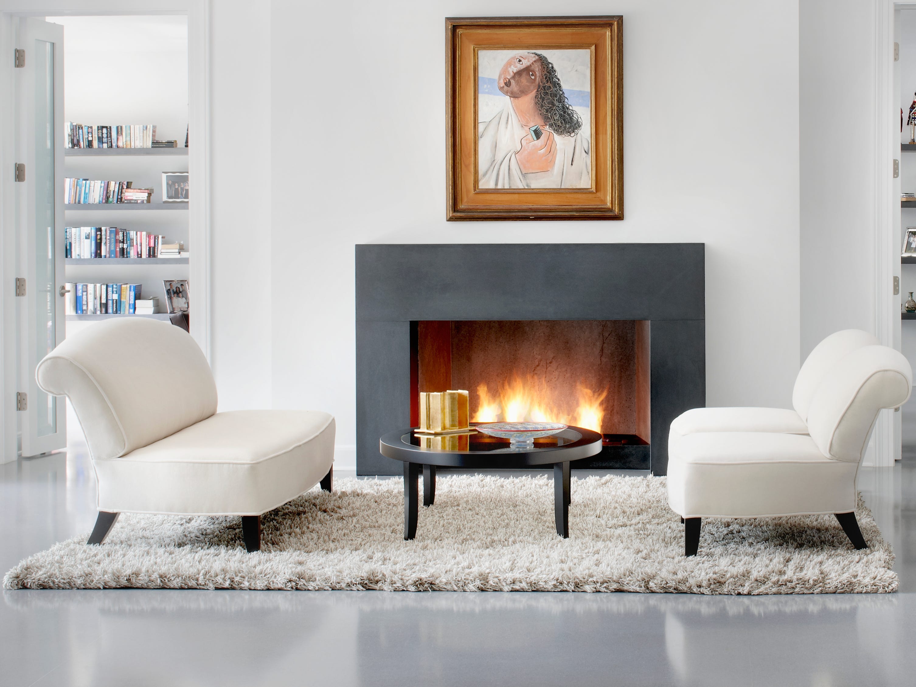 Warmweißes Wohnzimmer mit Shaggy-Teppich, cremeweißen Stühlen und einem Kamin mit einem Kunstwerk darüber, das einen abstrakten Mann darstellt