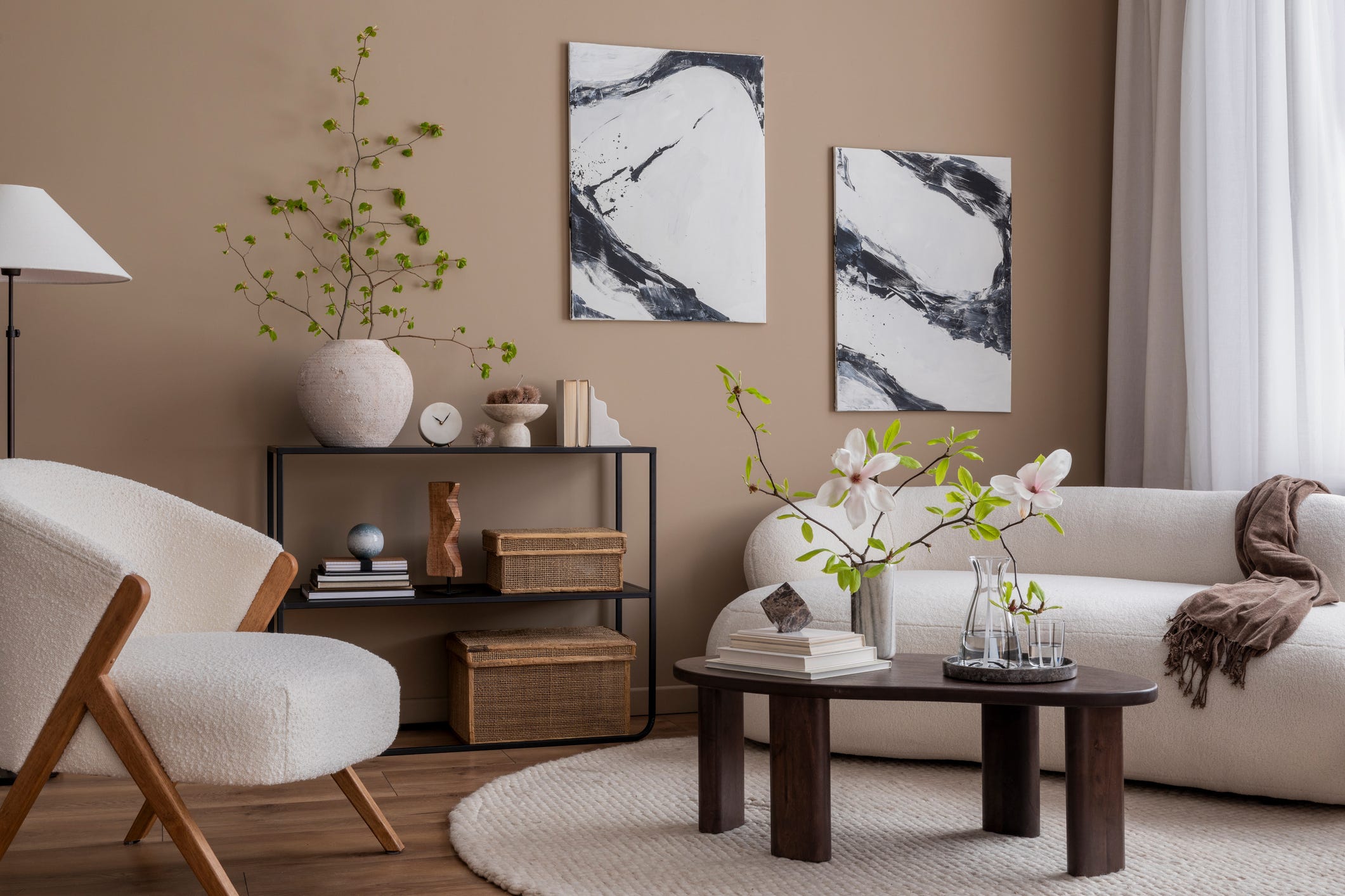 Wohnzimmer mit taupefarbenen Wänden, weißem Stuhl und Bouclé-Sofa, dunkelbraunem Couchtisch aus Holz, rundem Teppich, Magnolie und persönlichen Accessoires