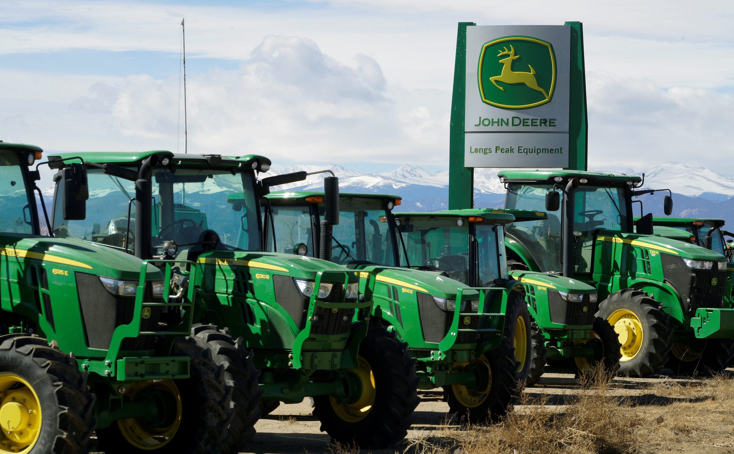 Reihe grüner John-Deere-Traktoren auf einem unbefestigten Grundstück mit schneebedeckten Bergen im Hintergrund