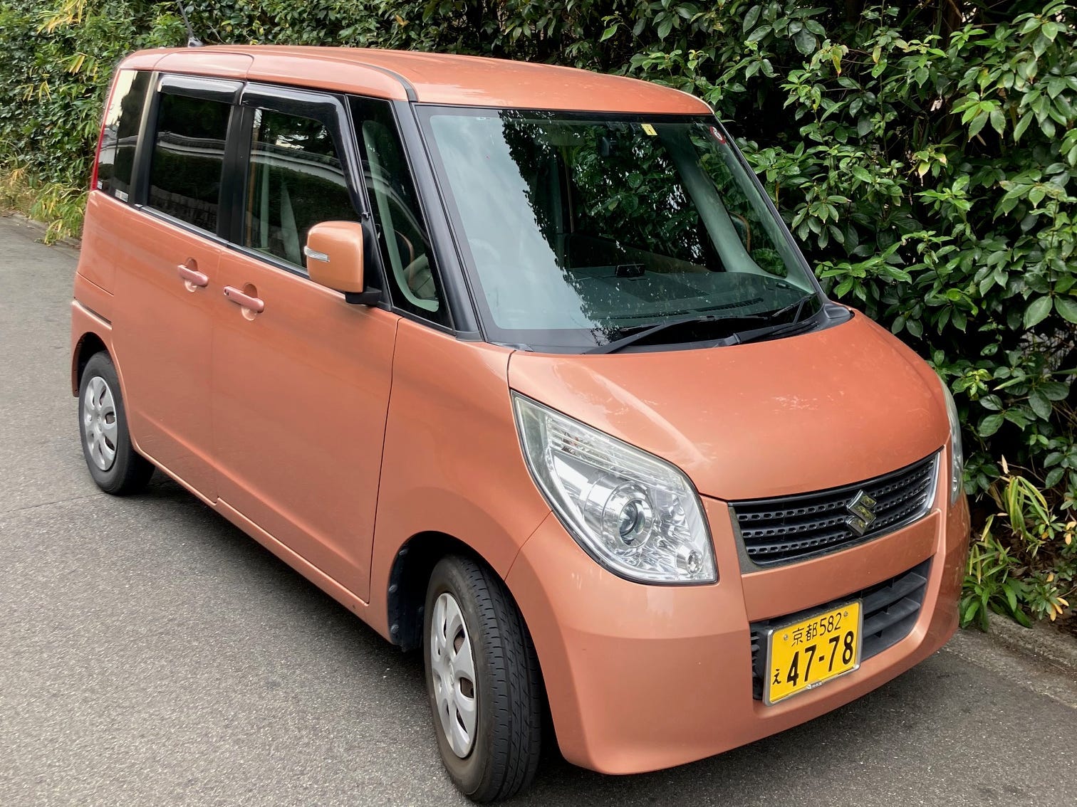 Ein Suzuki Palette Kei-Auto, das an einer Hecke in Japan geparkt ist