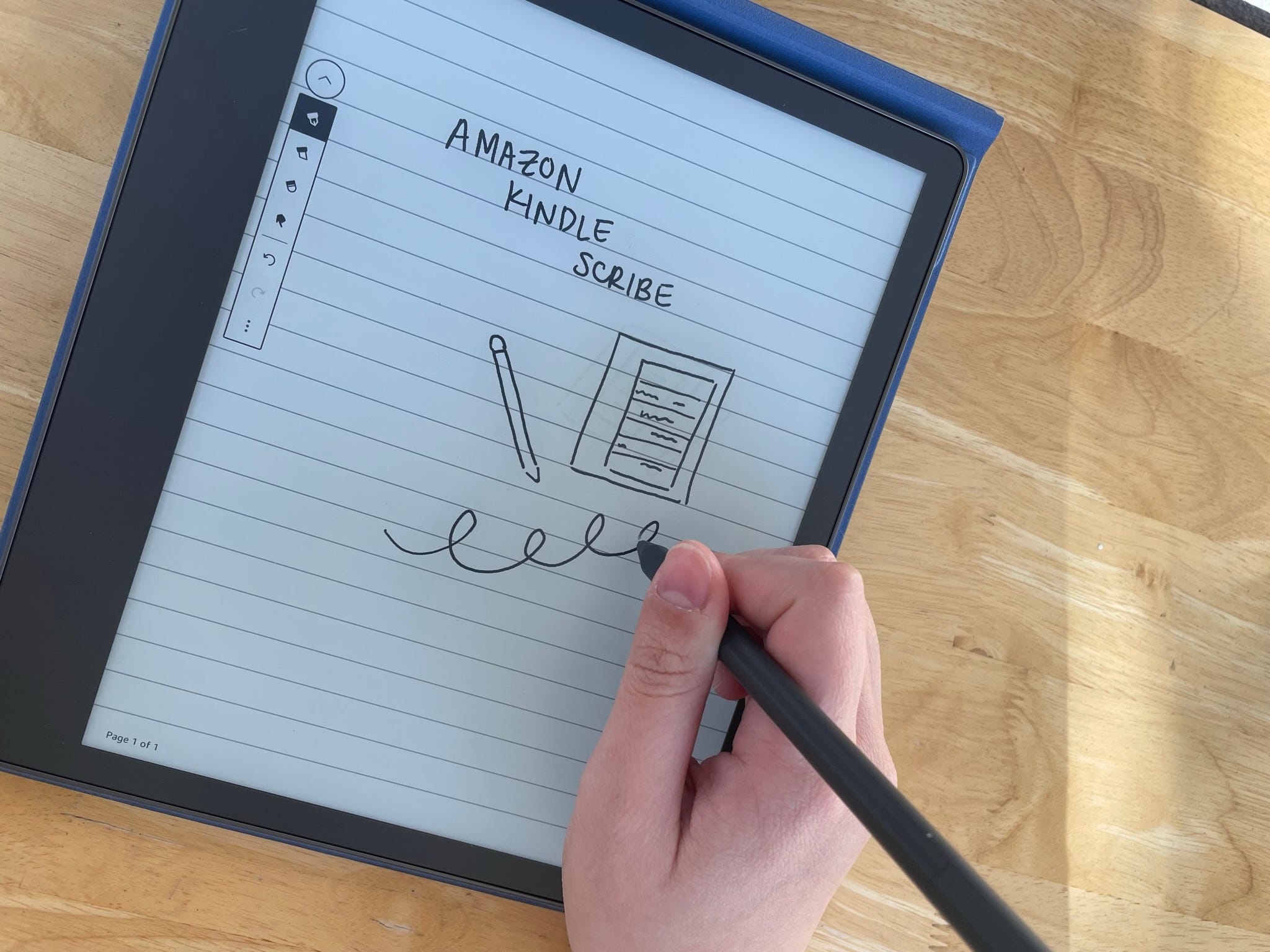 Ein Amazon Kindle Scribe, auf dem mit dem Stift auf einer Holzoberfläche geschrieben wird.