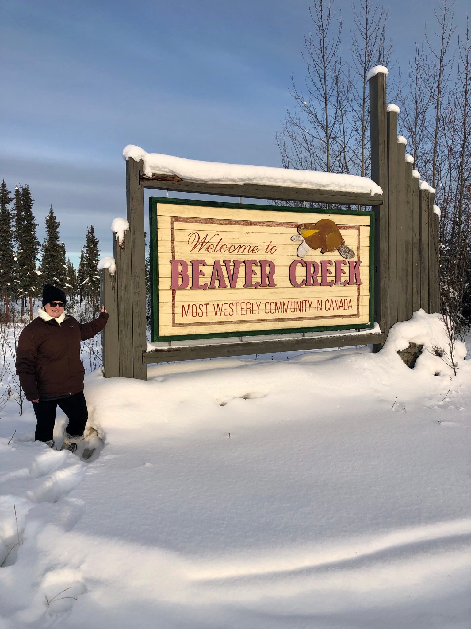 Eine Frau posiert im kniehohen Schnee vor einem Schild in Kanada.