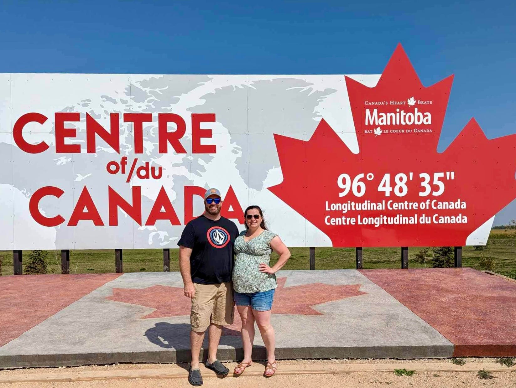 Ein Mann und eine Frau stehen vor einem Schild mit der Aufschrift „Centre of/du Canada“.