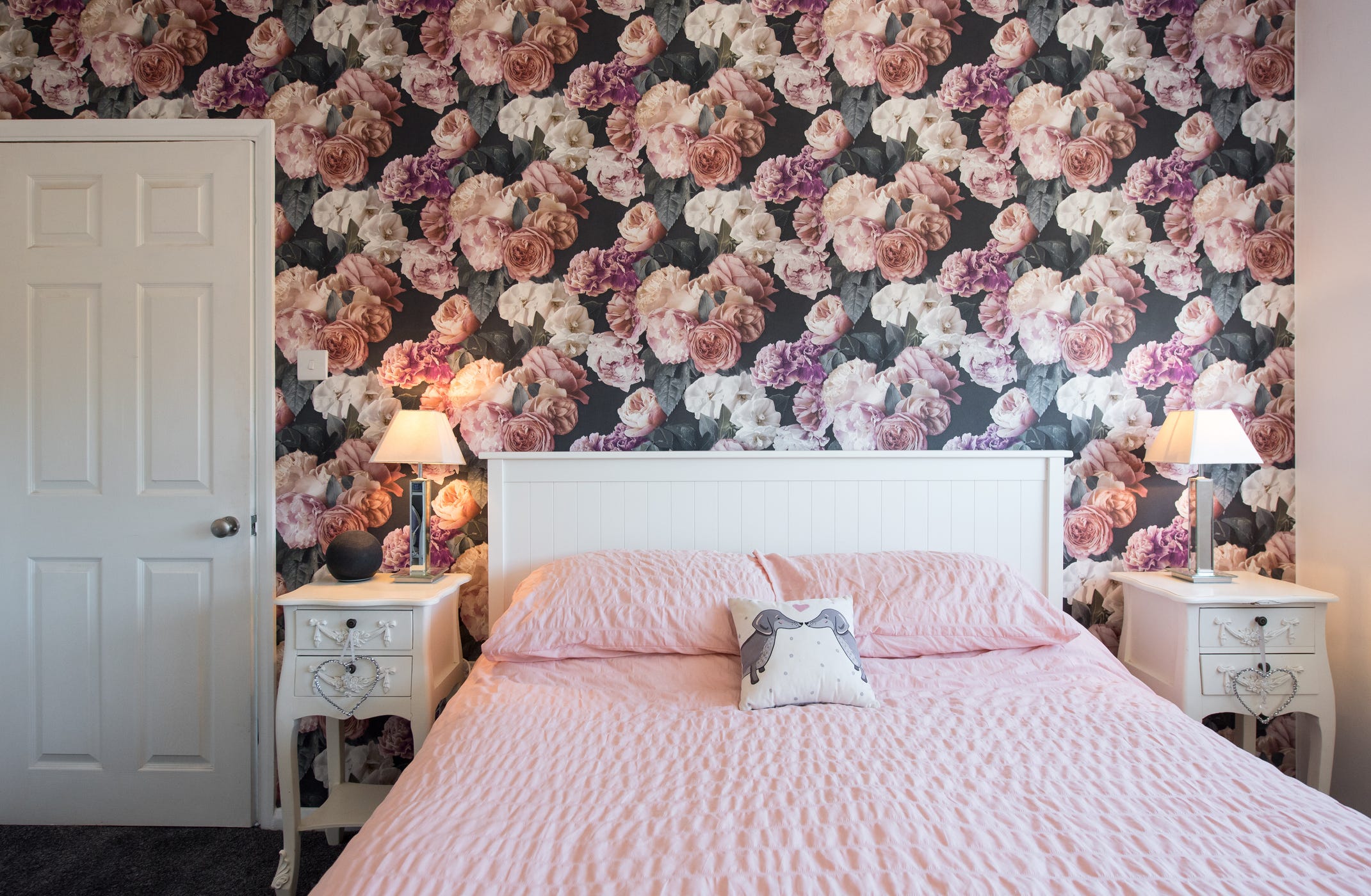 Blumentapete hinter weißem Bett mit rosa Laken