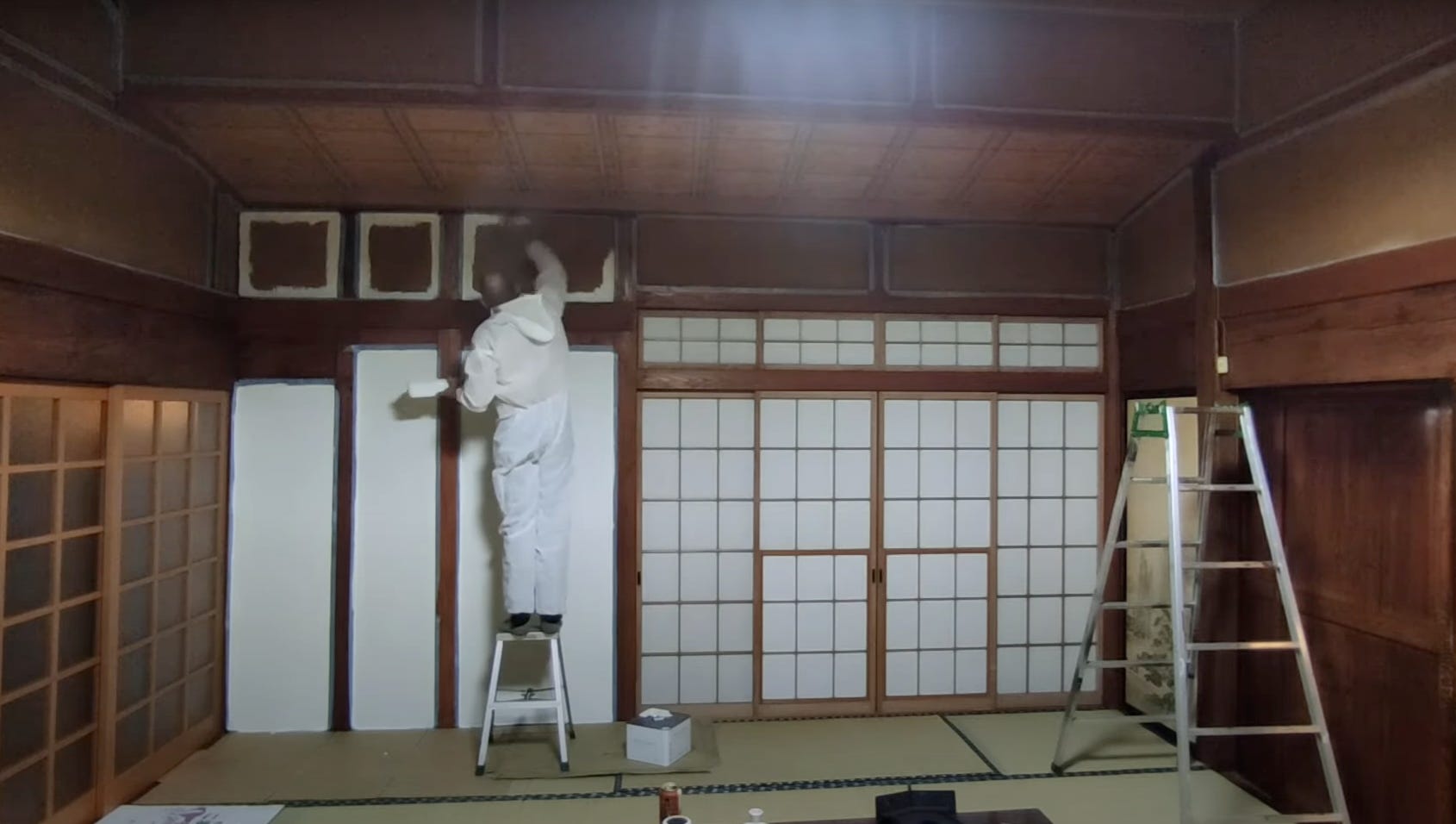 Ein Mann in einem Schutzanzug bemalt die Wände eines verlassenen Hauses auf dem japanischen Land.
