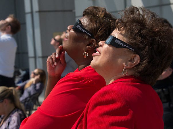 Zwei Frauen in rotem Hemd und eckiger Sonnenfinsternisbrille blicken ins Sonnenlicht