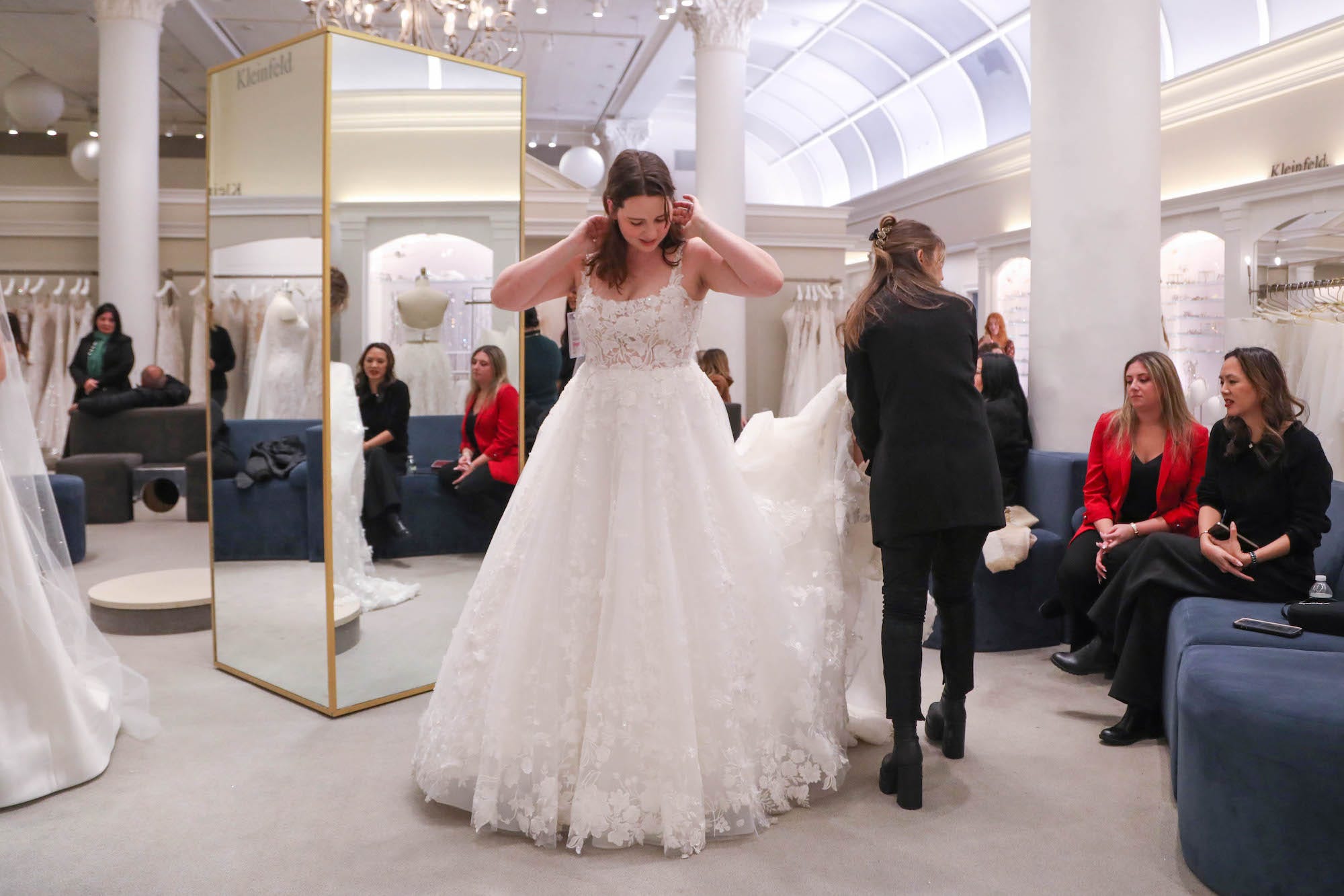 Eine Frau blickt auf ein Hochzeitskleid herab, das sie in einem Brautmodengeschäft anprobiert.