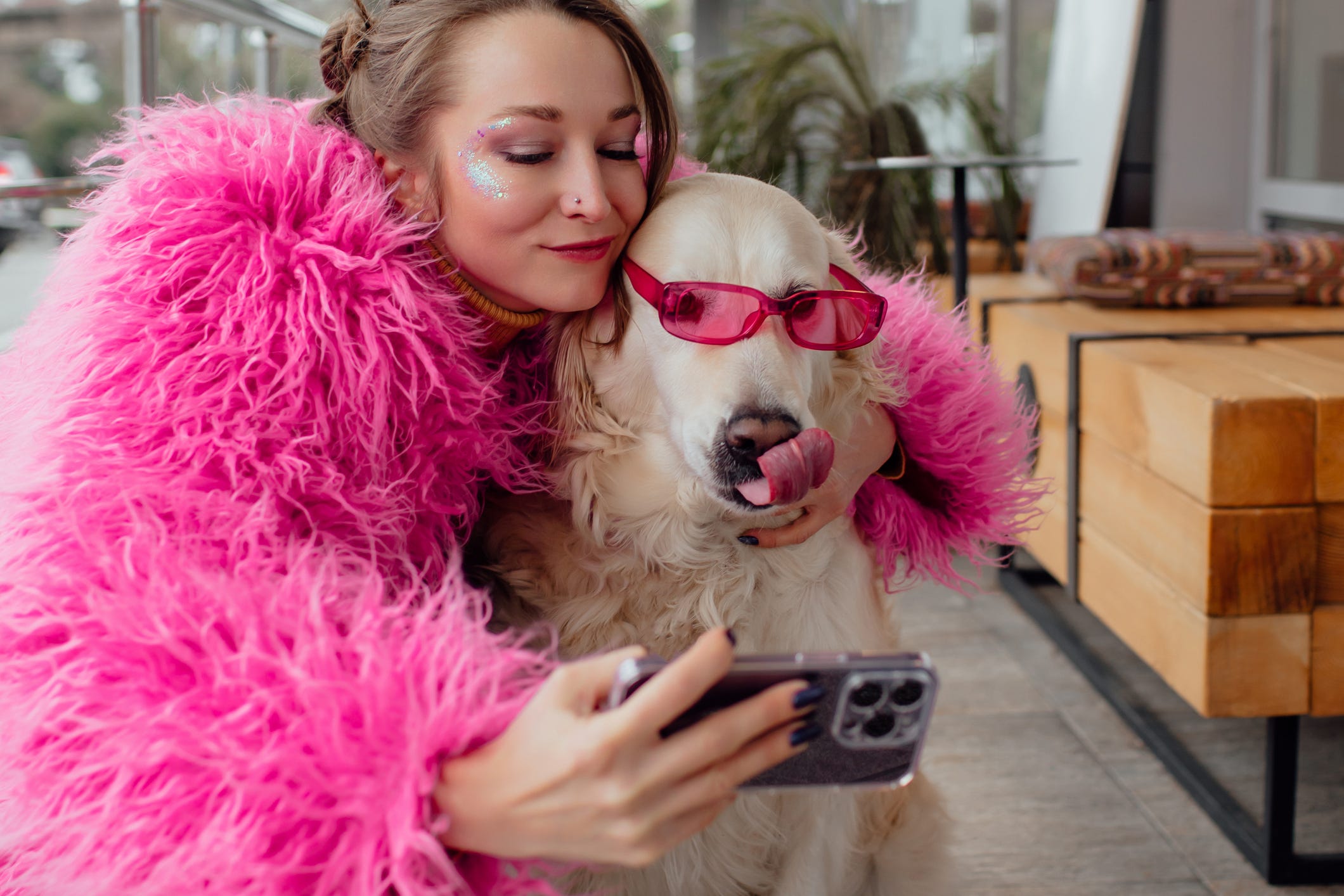Eine Frau in einem rosa flauschigen Pelzmantel macht ein Selfie mit ihrem Hund und einer rosa Sonnenbrille.