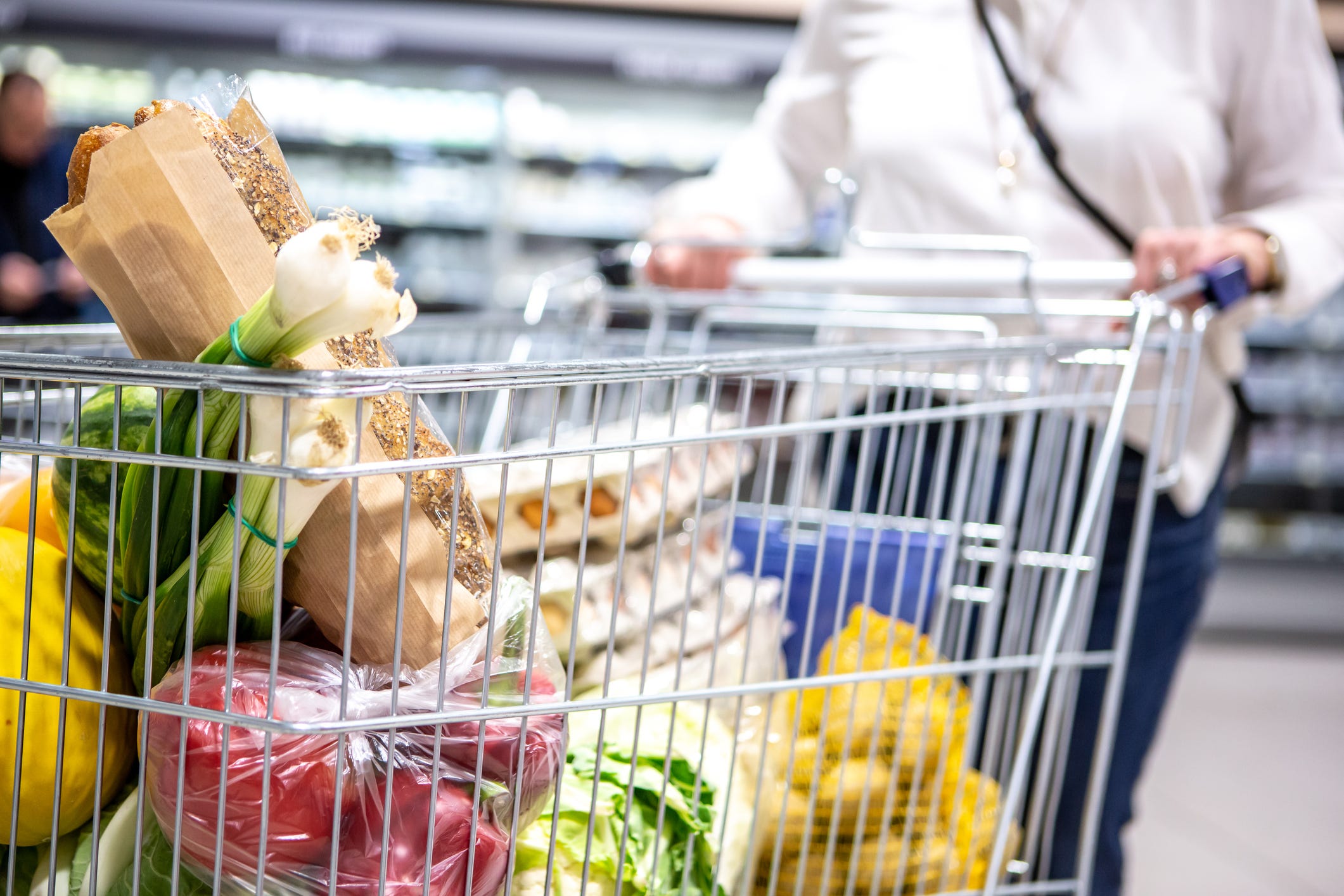 Frau schiebt einen Einkaufswagen in einen Supermarkt voller Brot, Eier und Gemüse