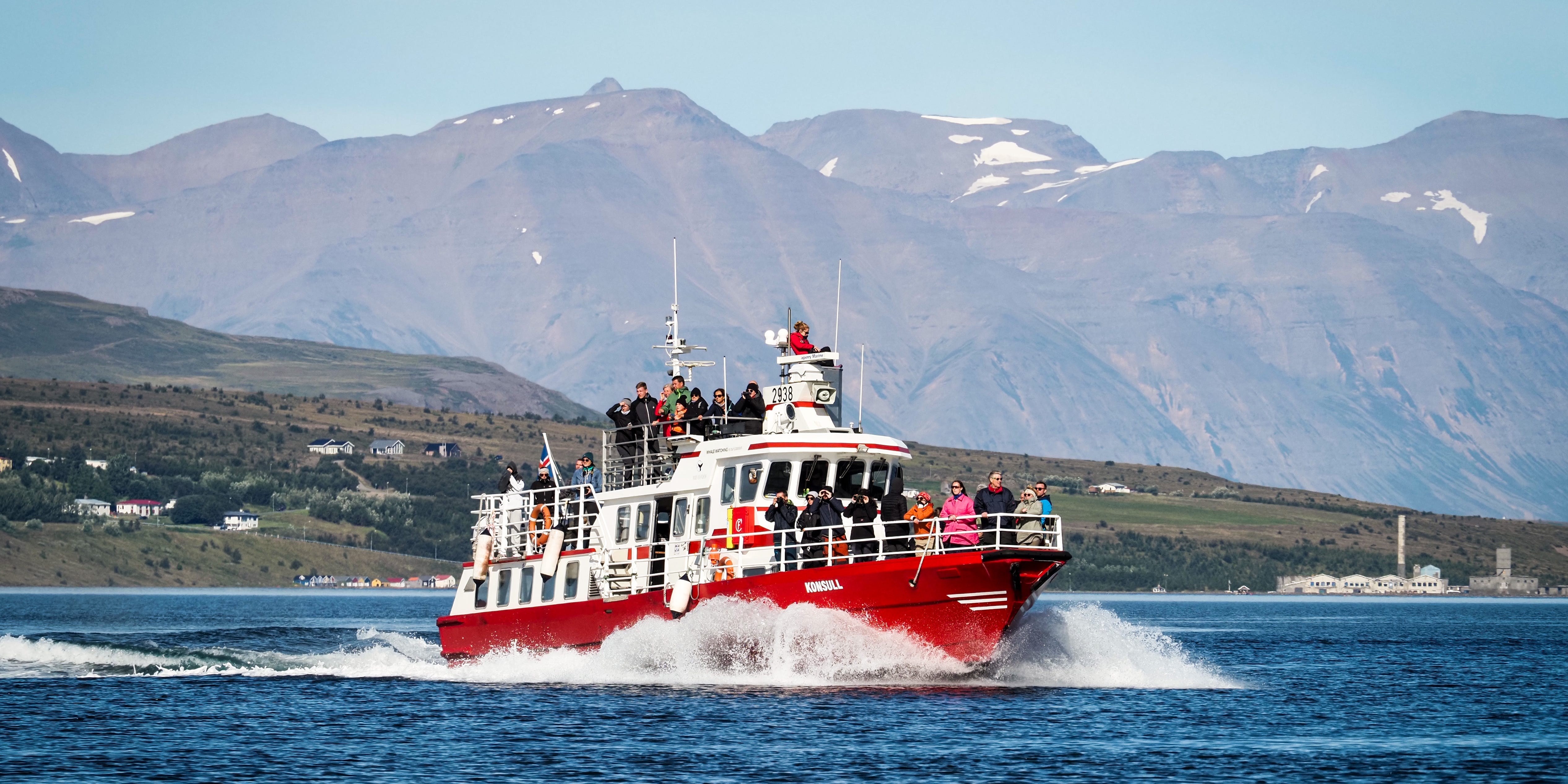 Das Schiff „Konsull“ mit Touristen an Bord fährt im Eyjafjördur-Fjord vor der Kulisse teilweise schneebedeckter Berge zur Walbeobachtung in Island