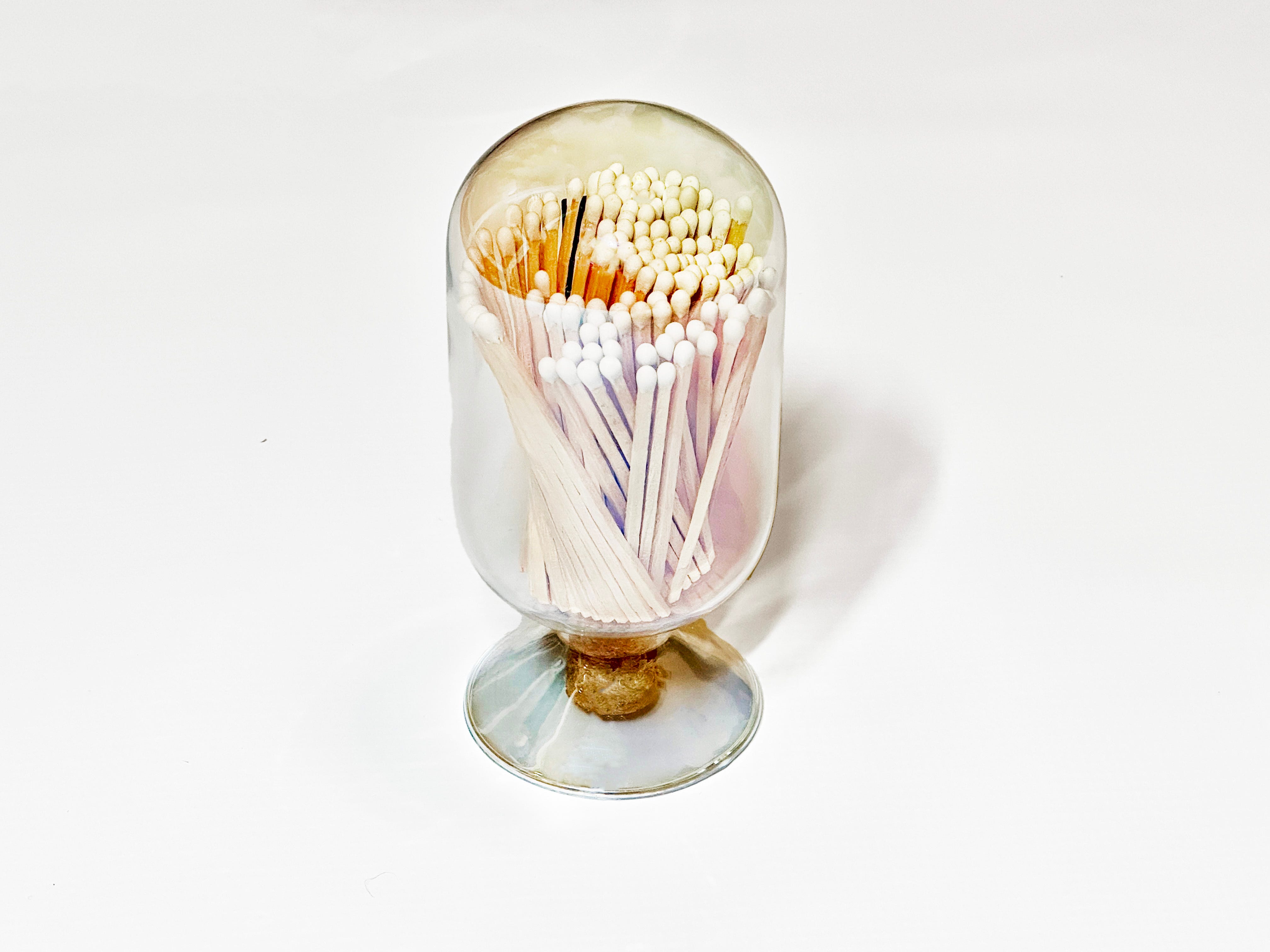 Eine dekorative Glocke aus durchsichtigem Glas hält Streichhölzer.  Die Cloche ist auf einem einfarbig weißen Hintergrund platziert