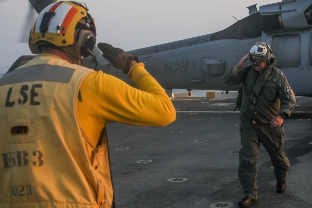 Ein Militärkapitän grüßt einen Flugdeckoffizier mit einem Hubschrauber hinter ihm