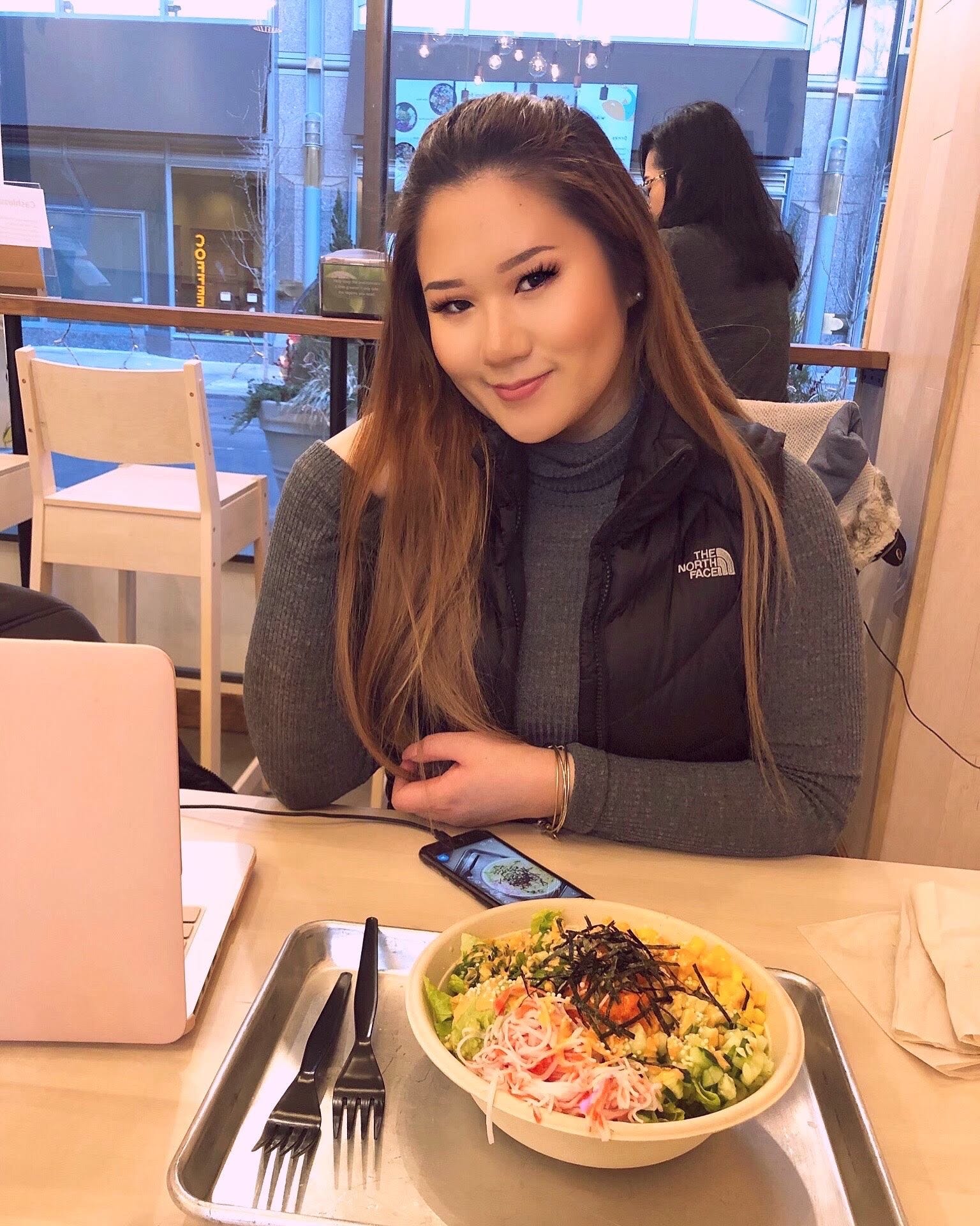 Kelsey Lam sitzt an einem Tisch in einem Restaurant.  Vor ihr steht ein Tablett mit einem Salat.