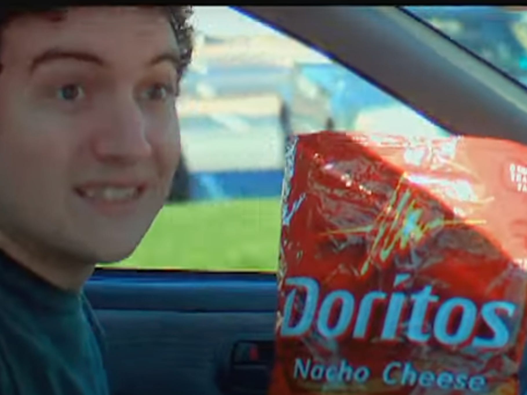 Mann lächelt, während er fährt, während er eine Tüte Doritos in der Hand hält.