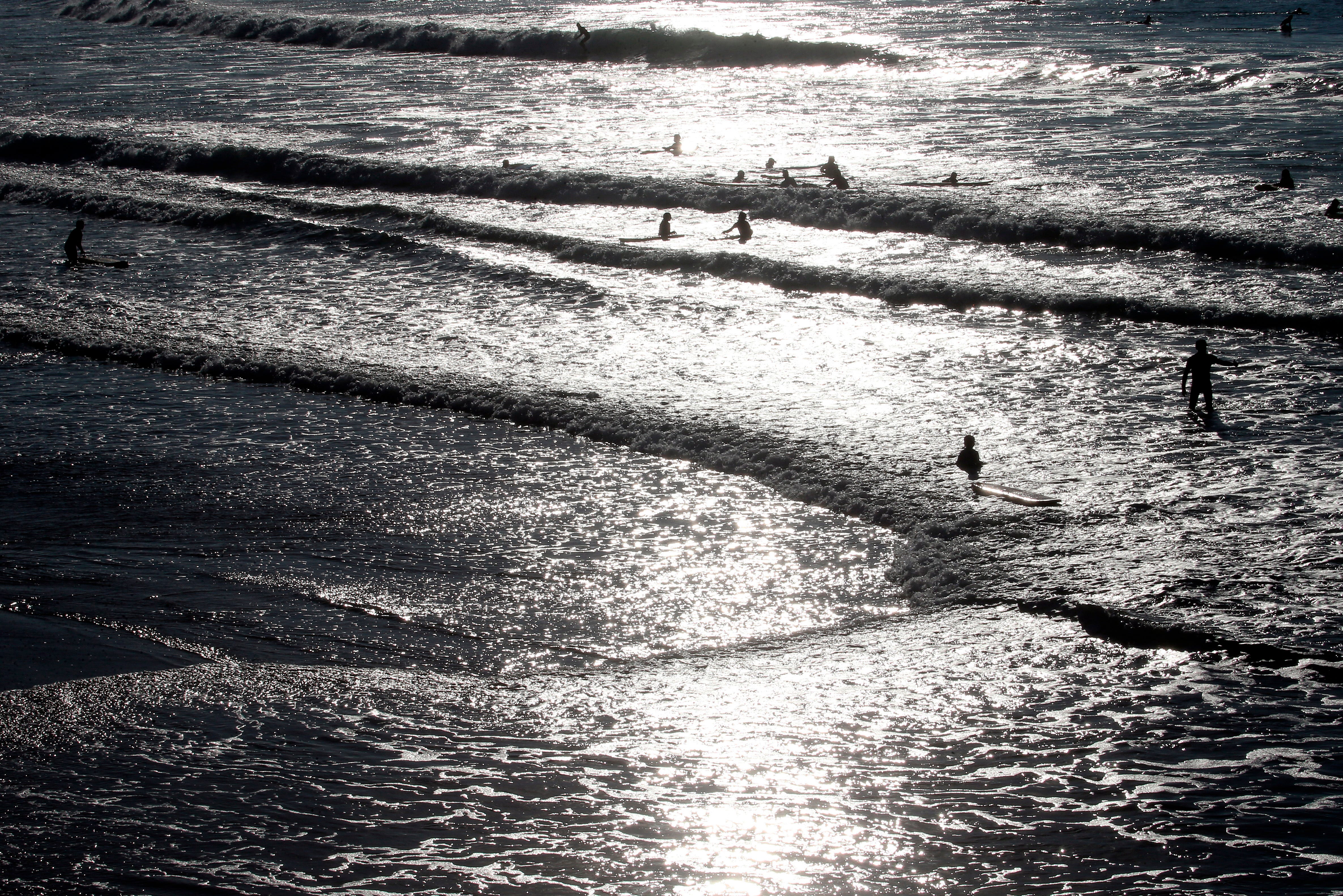 Menschen an einem Strand mit Sonnenlicht, das vom Wasser reflektiert wird, während Wellen an Land spülen