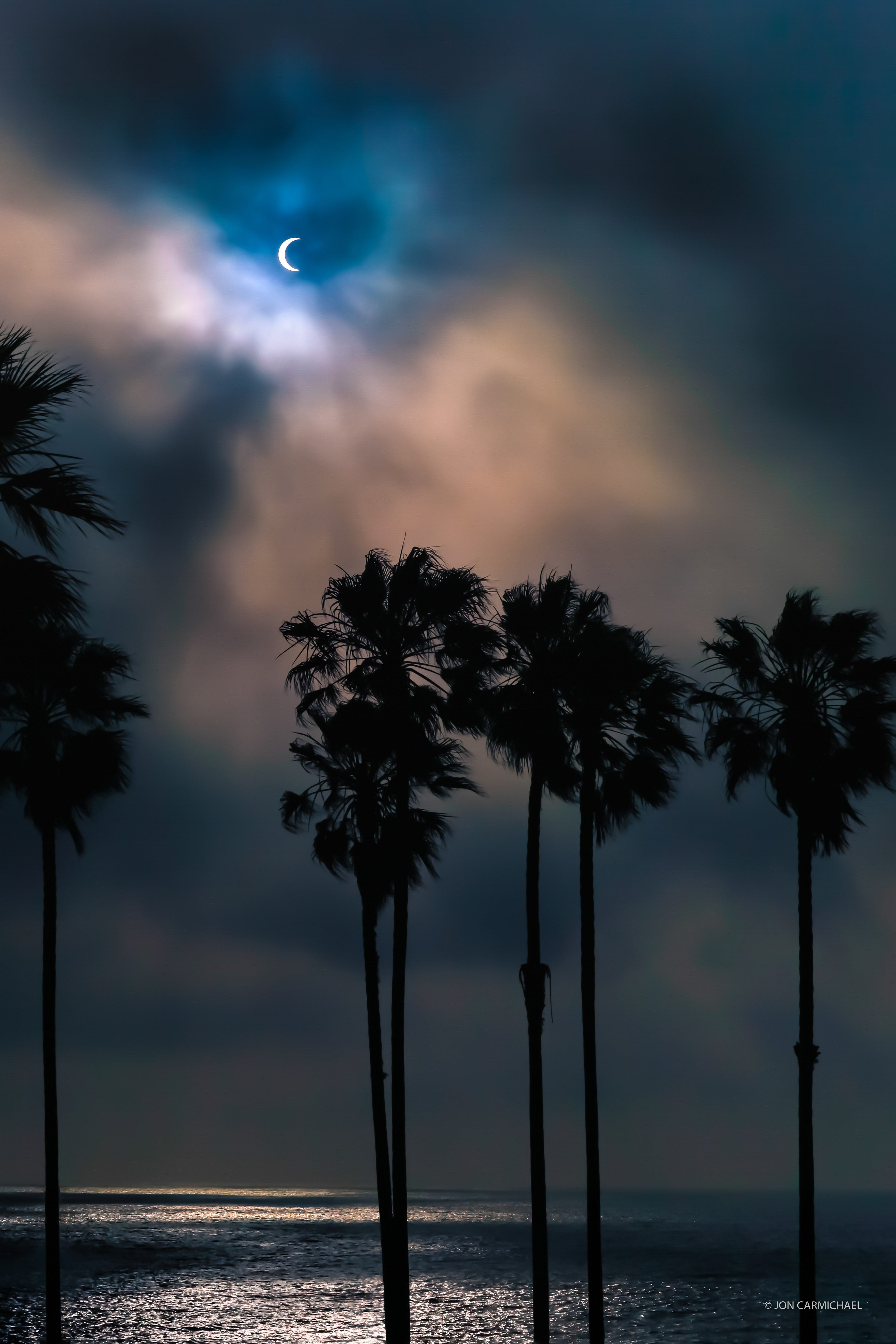 Der Mond verdunkelt teilweise die Sonne am Himmel mit Palmen und dem Meer im Vordergrund.