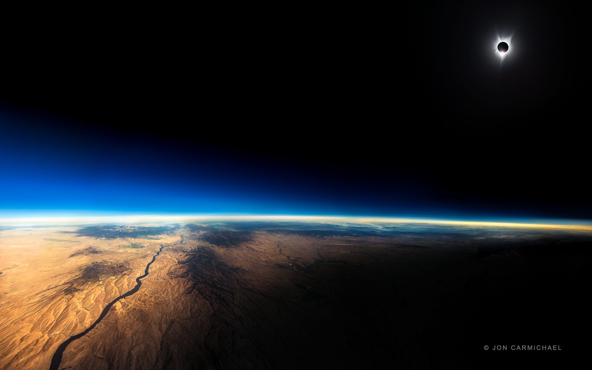 Totale Sonnenfinsternis oben rechts im Foto, wobei der Schatten des Mondes auf das bergige Land darunter fällt.