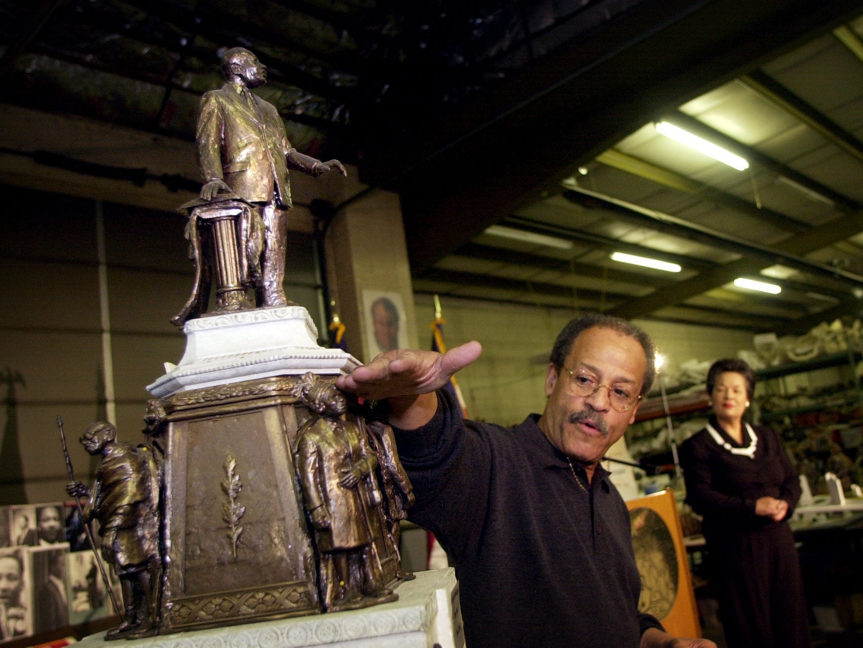 Ed Dwight deutet auf eine Bronzestatue, die er geschaffen hat, während eine Frau in der Ferne zuschaut