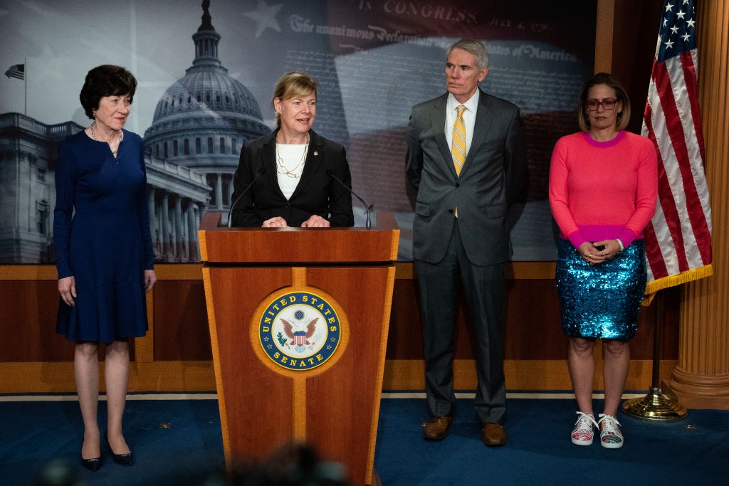 Sens. Tammy Baldwin (D-WI), Susan Collins (R-ME), Rob Portman (R-OH) und Kyrsten Sinema (D-AZ) nehmen an einer Pressekonferenz teil.  Sinema trägt einen pinkfarbenen Pullover und einen blaugrünen, glitzernden Rock