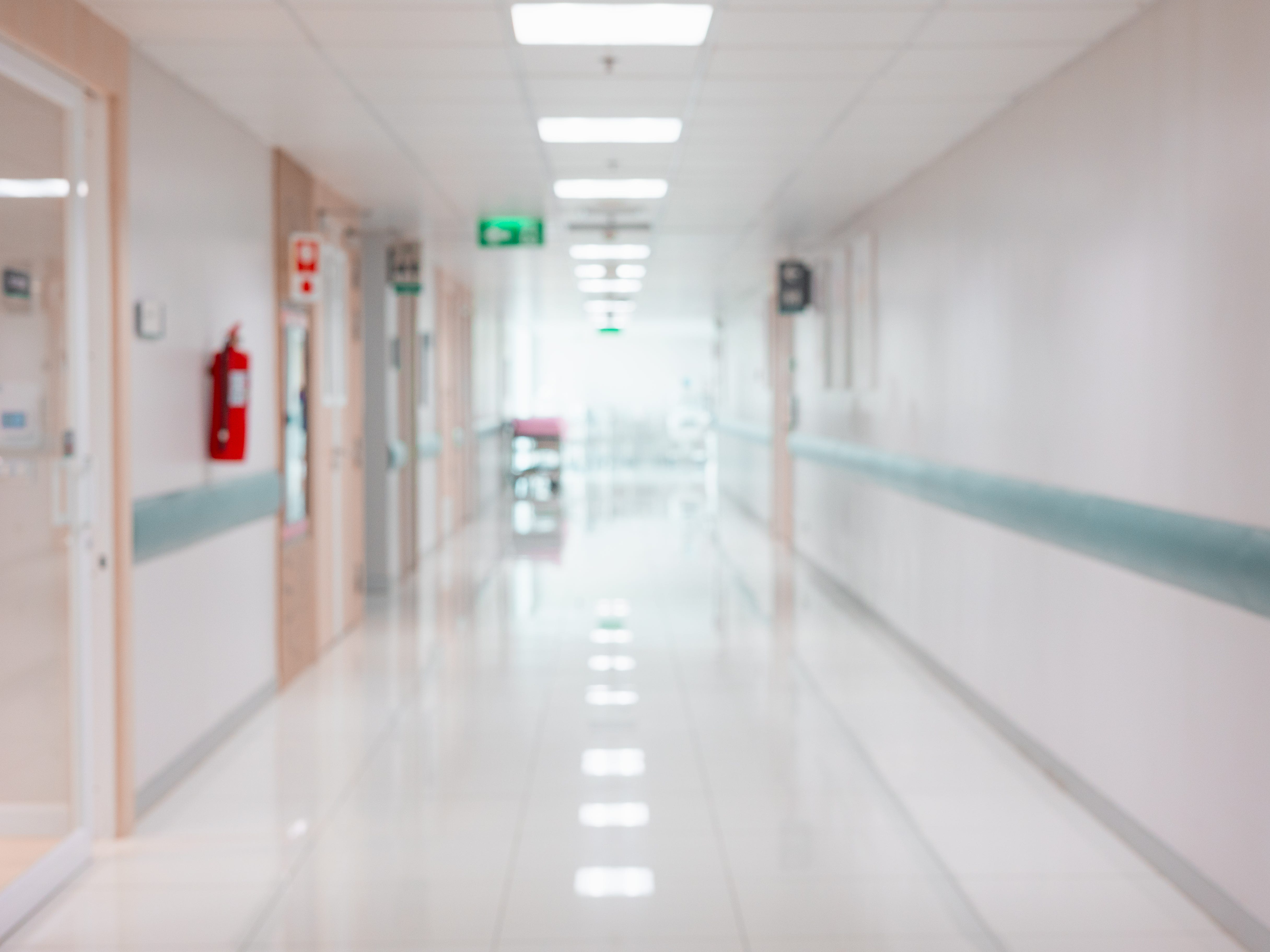 Ein leerer Krankenhausflur mit einem hellen Ausgangsschild neben einer Tür.