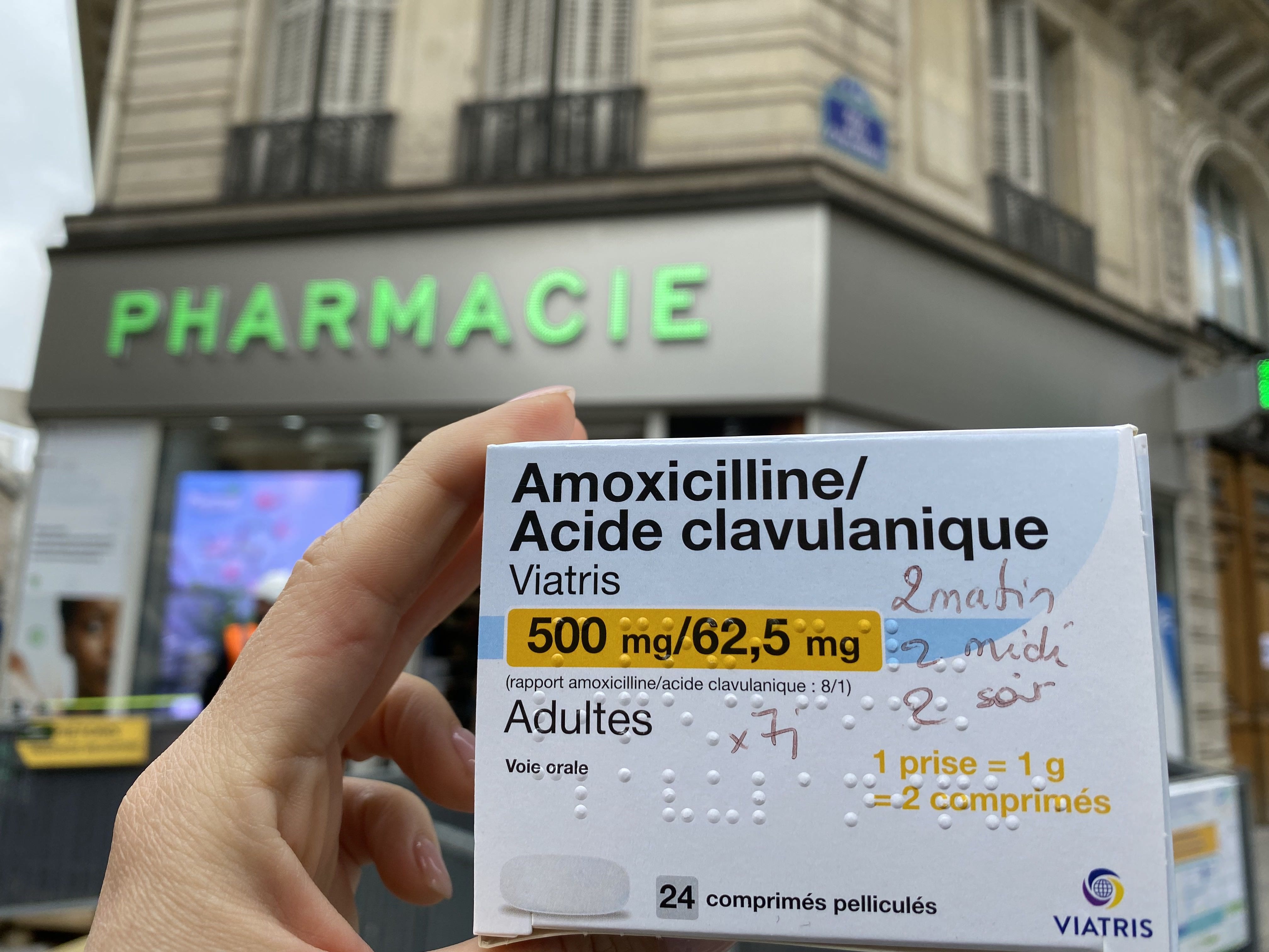 Der Autor hält eine Schachtel Pillen mit hübscher französischer Aufschrift auf der Vorderseite hoch, während er vor einer Apotheke steht