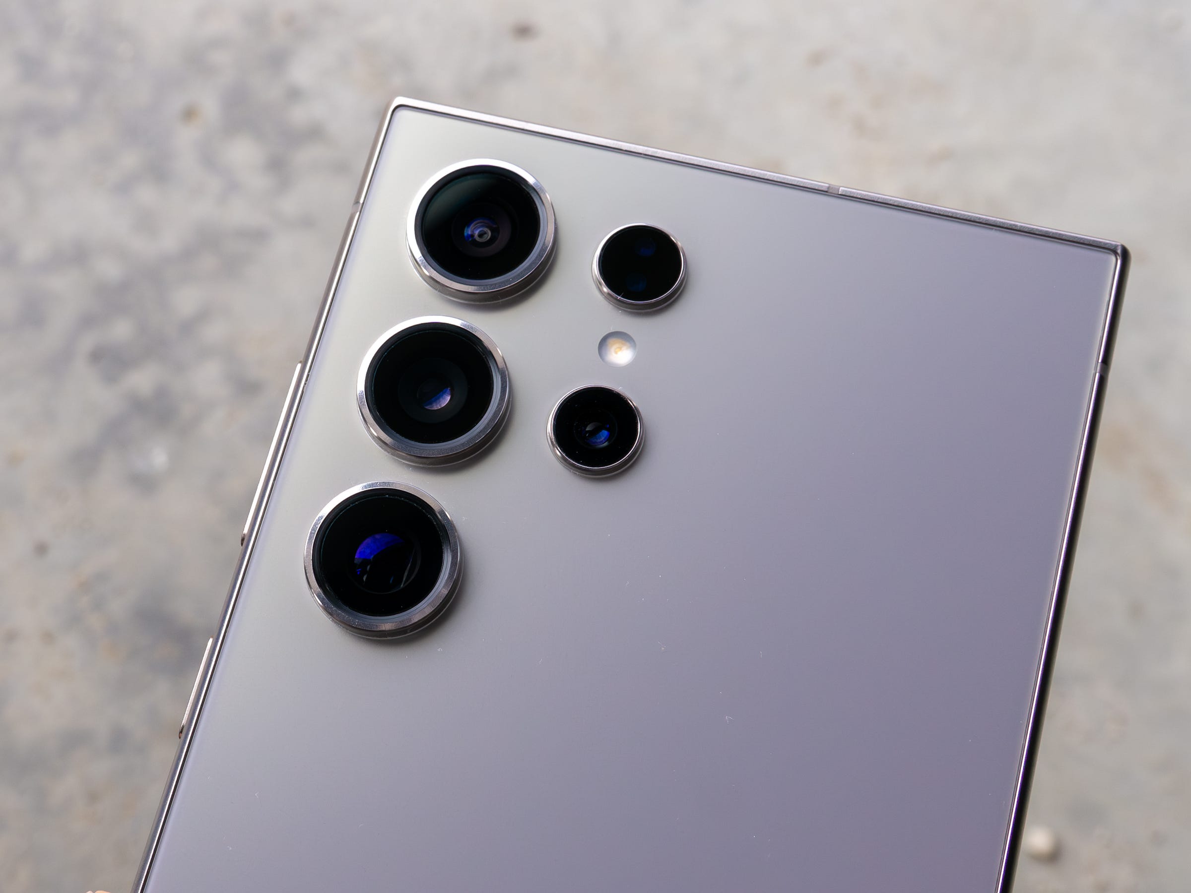 Eine Nahaufnahme der vier Kameras des Samsung Galaxy S24 Ultra, aufgenommen vor einem grauen Zementhintergrund.