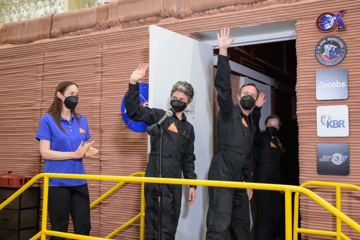Drei Menschen in Schwarz winken im Eingang eines wohnwagengroßen Gebäudes, während eine Frau in Blau klatscht