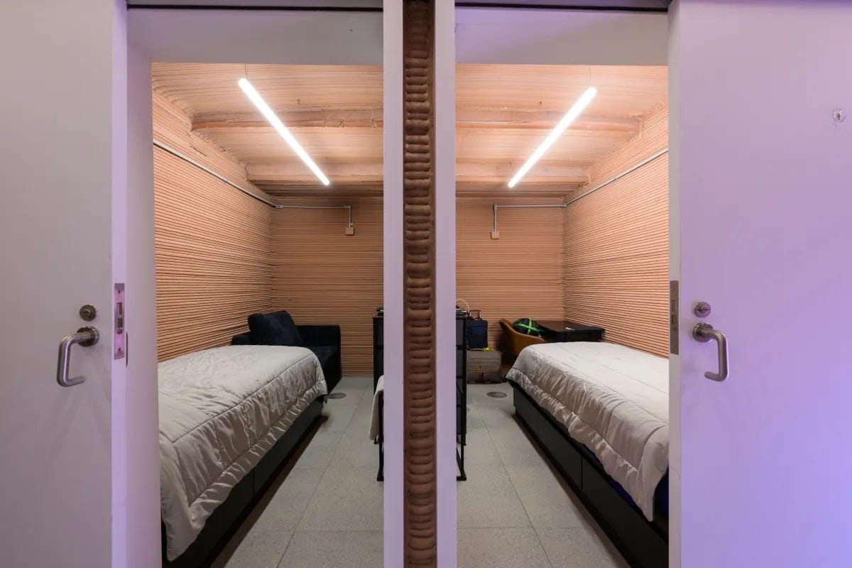 Offene Türen führen zu zwei identischen Schlafzimmern mit zwei Einzelbetten, Holzlattenwänden und einer LED-Deckenleuchte