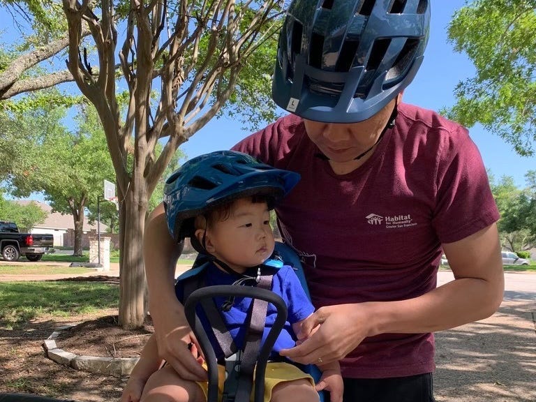 Cheng umarmt seinen Sohn, der auf einem Fahrrad sitzt.