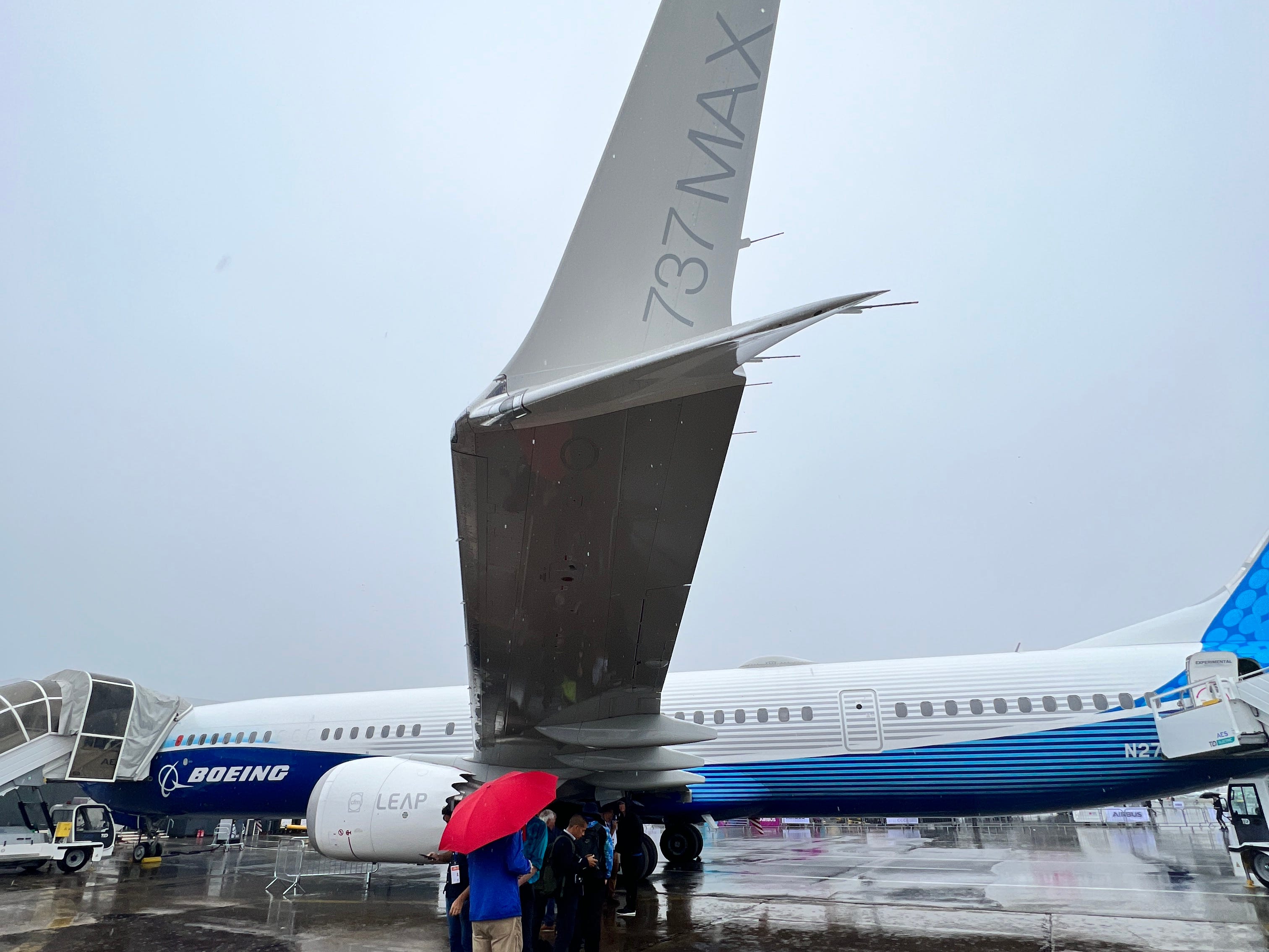Eine Boeing 737 Max 10 auf der Paris Air Show, mit Menschen, die unter dem Flügel Schutz vor dem Regen suchen, und dem Winglet mit dem 737 MAX-Logo im Vordergrund