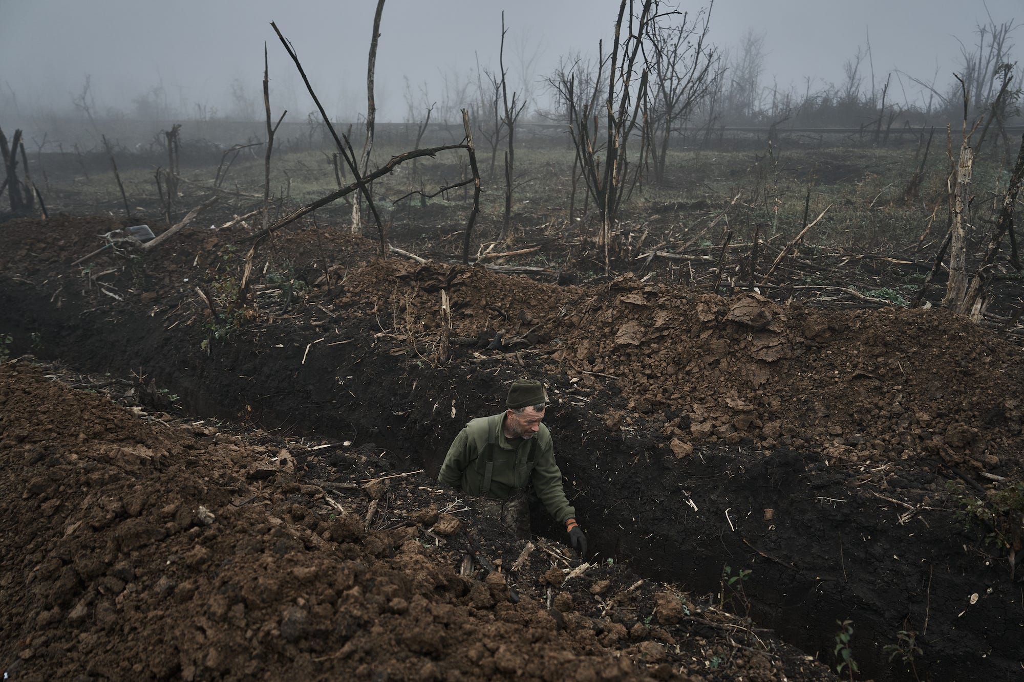 Ein ukrainischer Soldat in einem Schützengraben, umgeben von Nebel und verbrannten Bäumen