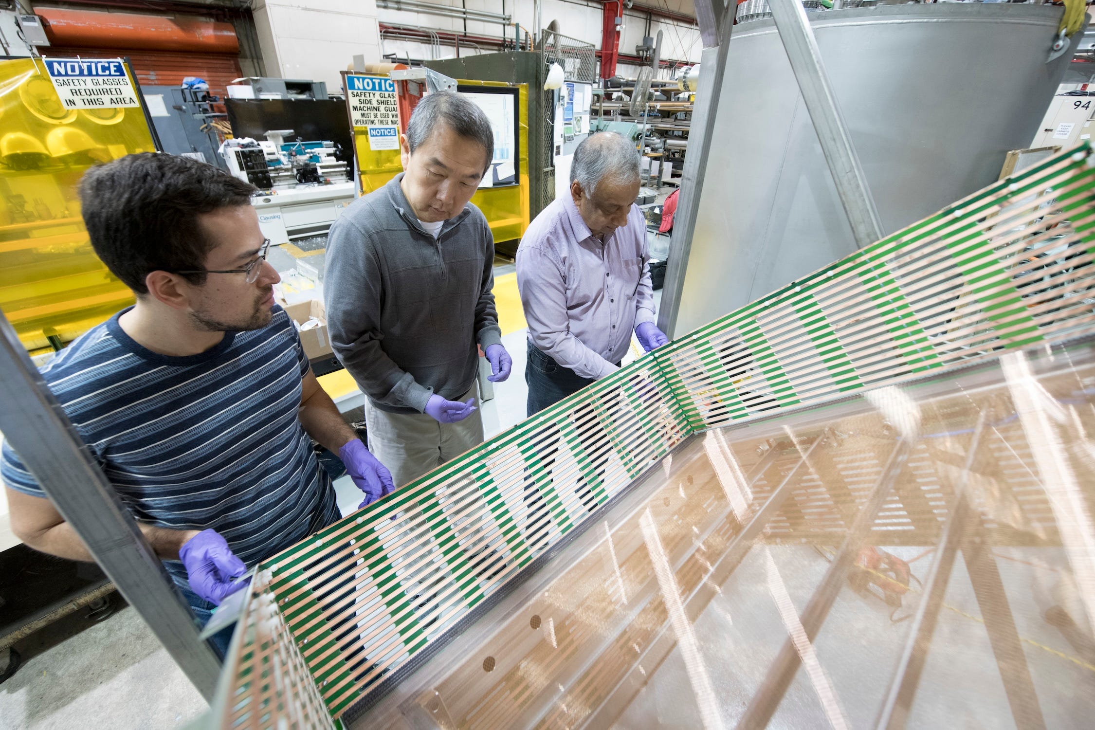 Drei Forscher betrachten ein großes reflektierendes elektronisches Gerät, das wie ein Glasrechteck aussieht