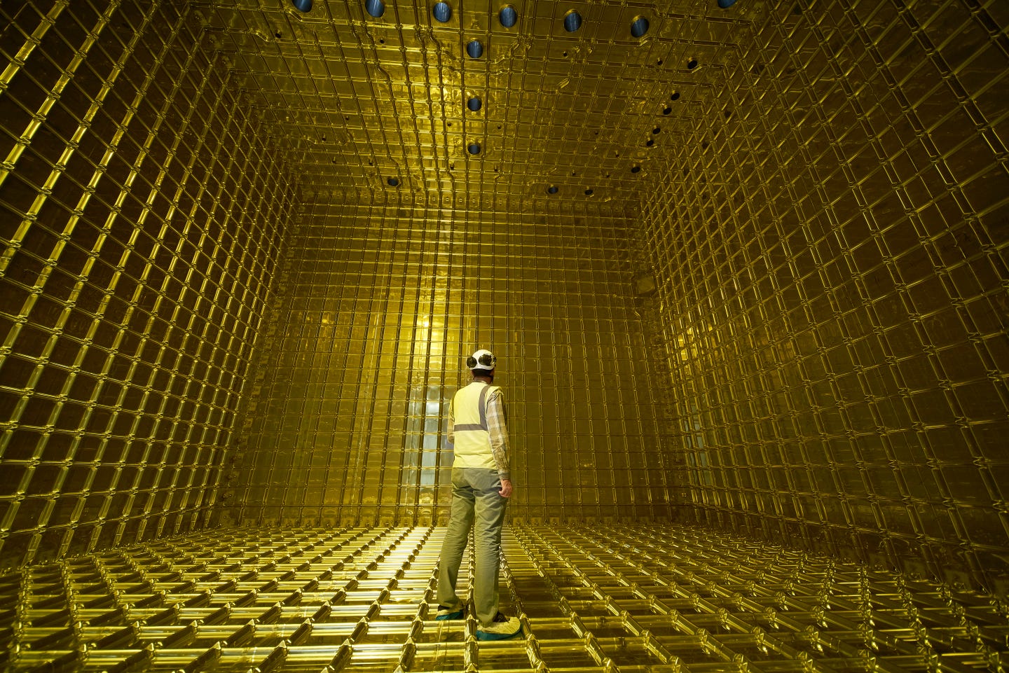 Eine Person mit Schutzhelm steht in einem goldenen Raum, dem protoDUNE-Experiment