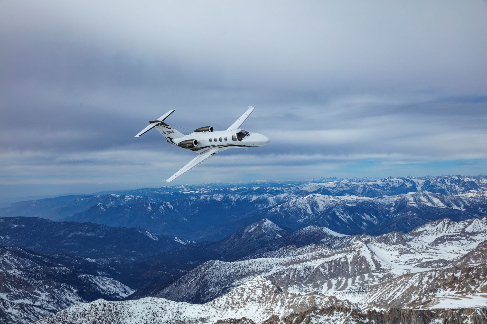 Cessna Citation M2 fliegt über schneebedeckte Berge.