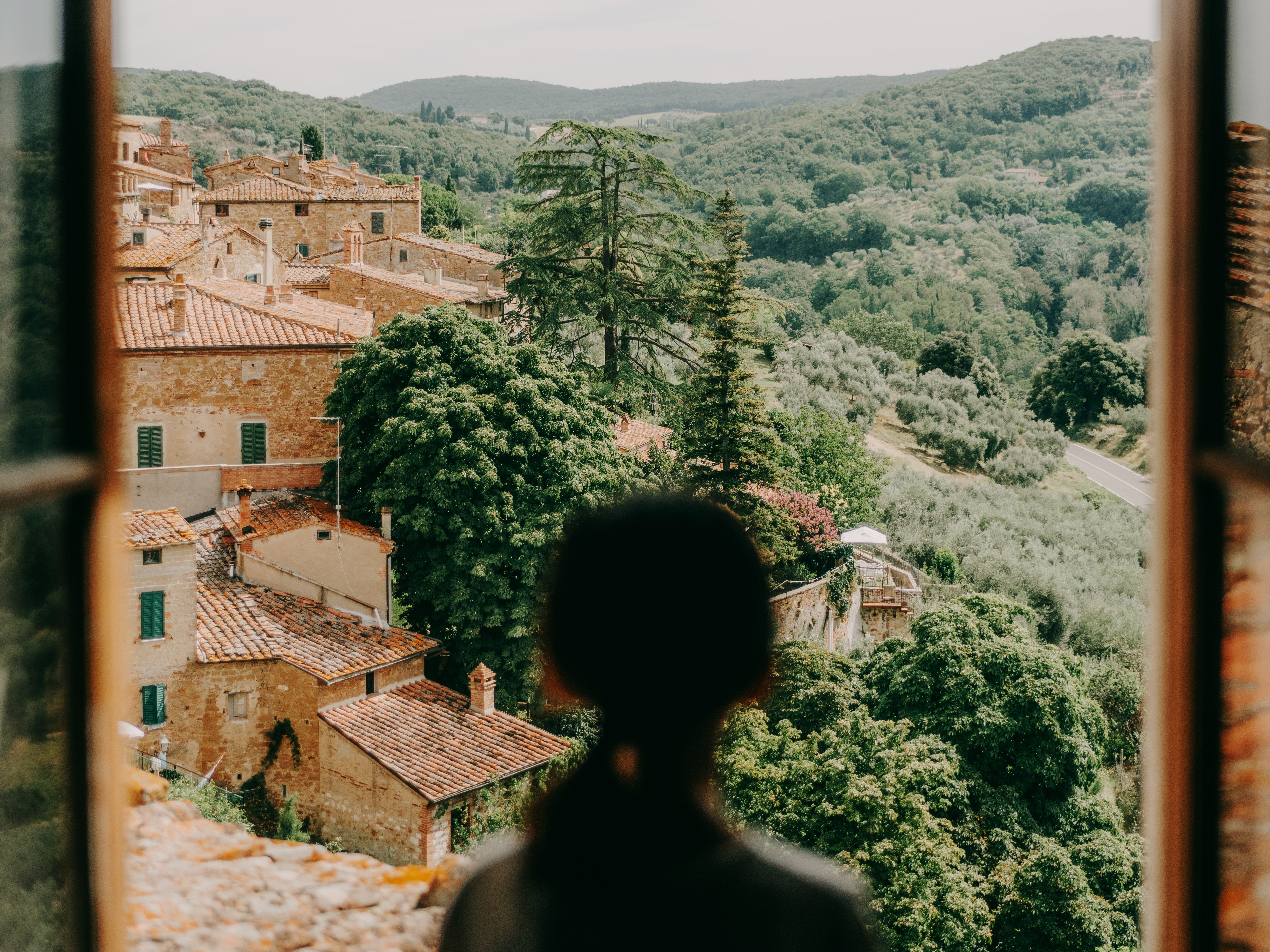 Person, die aus dem Fenster auf eine malerische Aussicht auf die Toskana blickt.