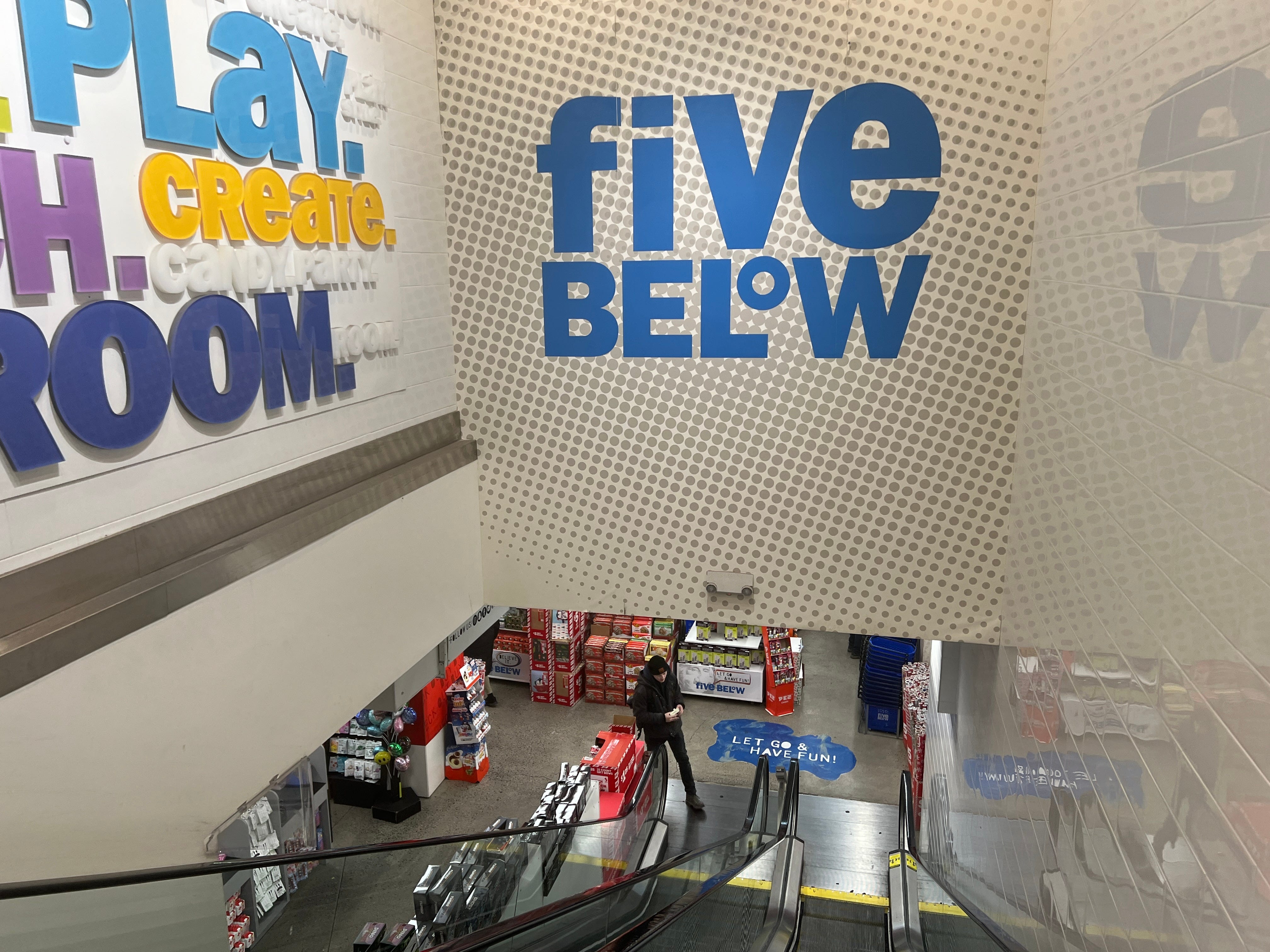 Ein Blick auf das Five Below-Logo an einer Wand über einer Rolltreppe im Geschäft.