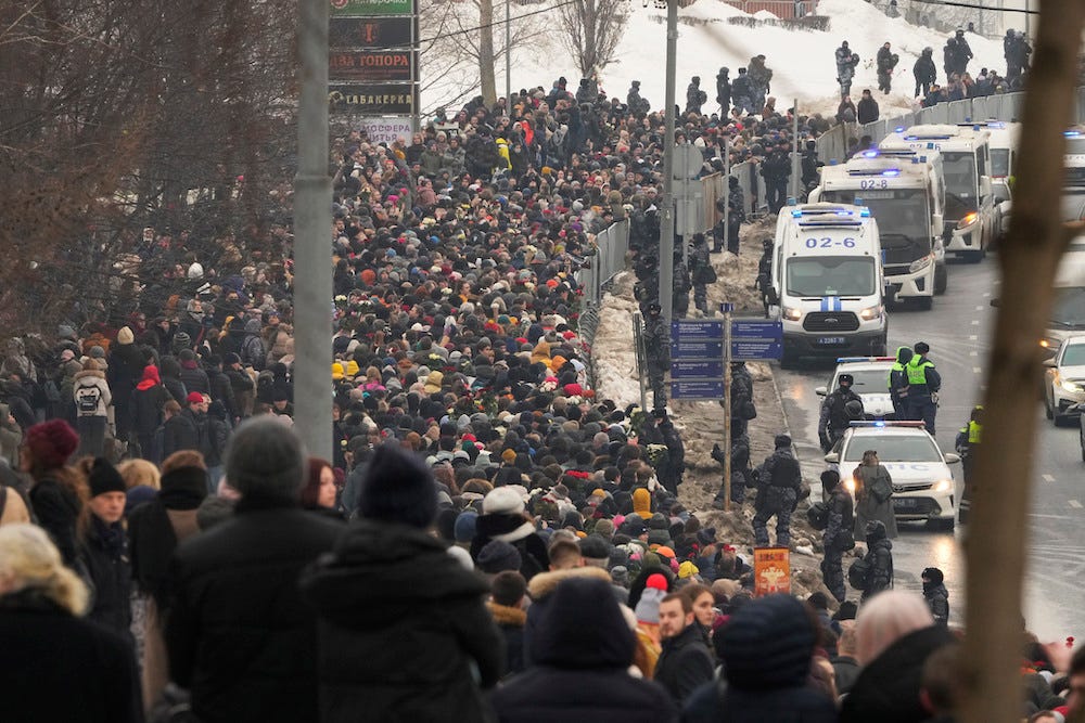 Eine Seitenansicht von Hunderten Schaulustigen an einem verschneiten Tag in Moskau, Russland, entlang einer Straße, auf der mehrere Polizeifahrzeuge den Leichnam des russischen Dissidenten Alexej Nawalny zu seiner Beerdigung am 1. März 2024 eskortieren.