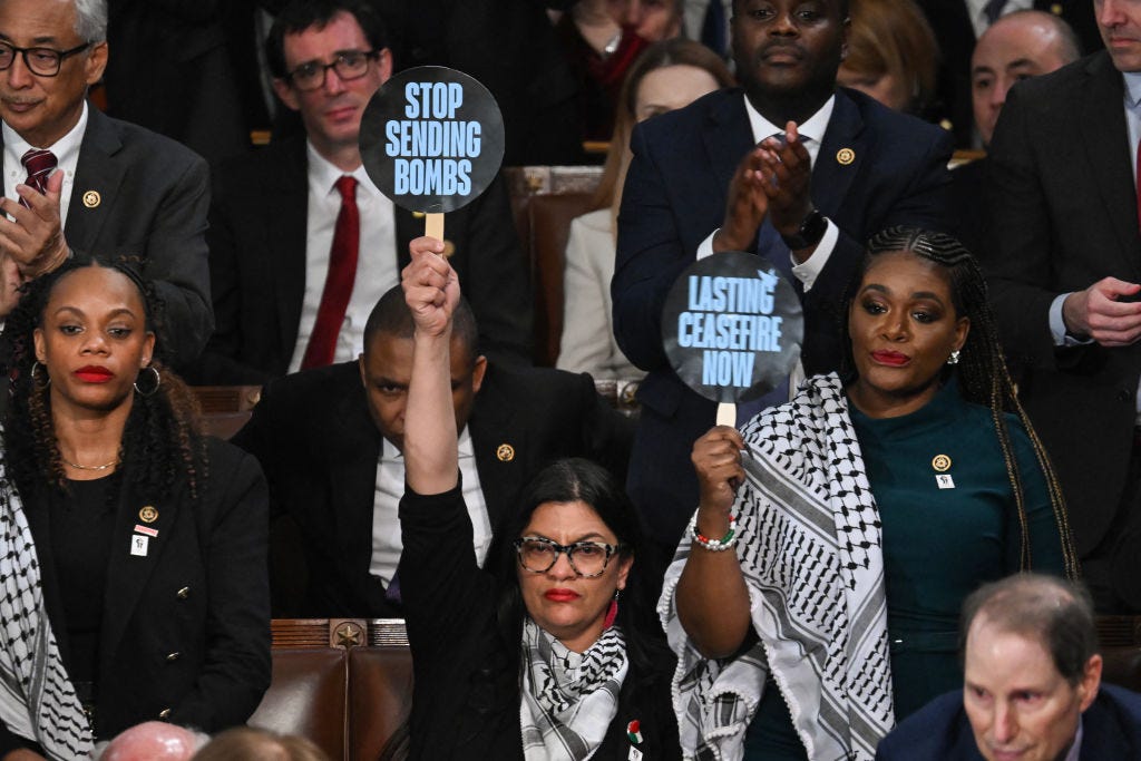 Rashida Tlaib und Cori Bush halten bei der Lage der Nation 2024 Schilder mit der Aufschrift „Stoppen Sie das Bombenschießen“ und „Jetzt dauerhaften Waffenstillstand“ hoch