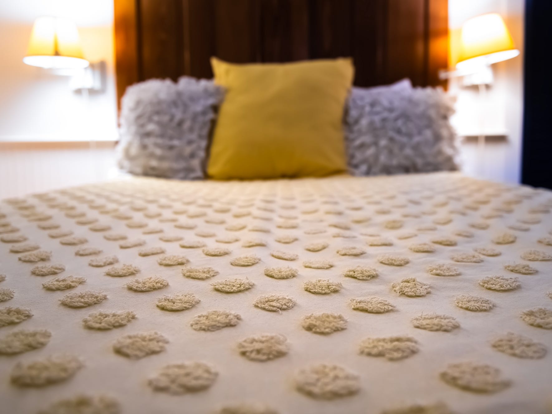 Bett mit einer strukturierten Tagesdecke mit Punkten und gelben und violetten Kissen