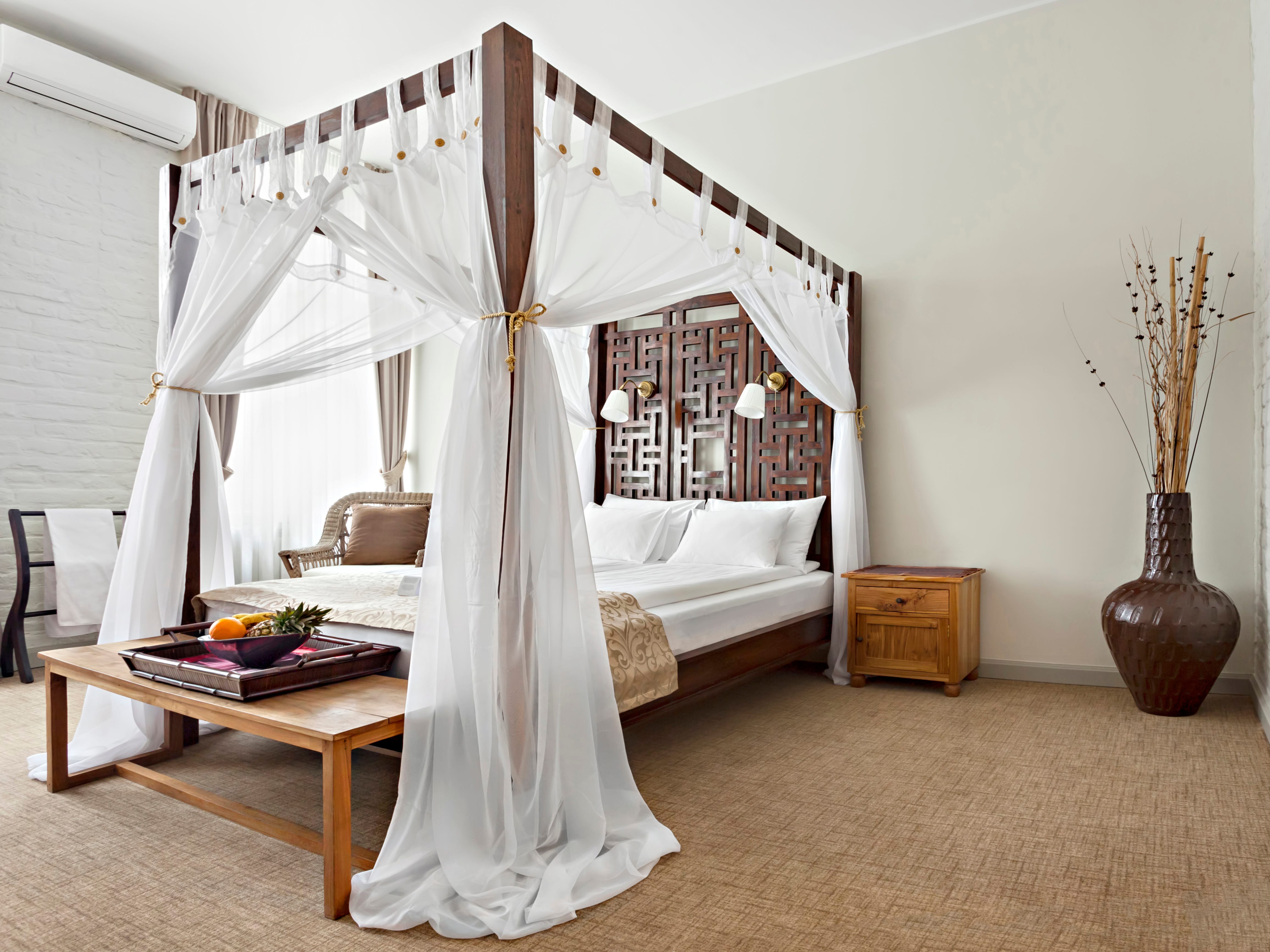 Sauberes, neutrales Schlafzimmer mit einem großen hölzernen Himmelbett mit transparenten weißen Vorhängen
