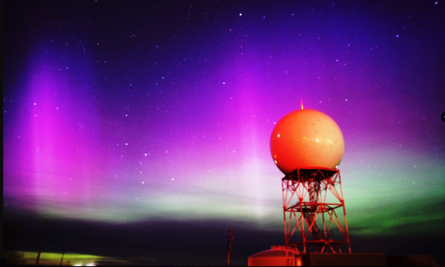 Ein Bild des nationalen Wetterdienstes von Riverton in Wyoming zeigt violette und grüne Nordlichter, die hinter einer kugelförmigen Struktur im Vordergrund leuchten.