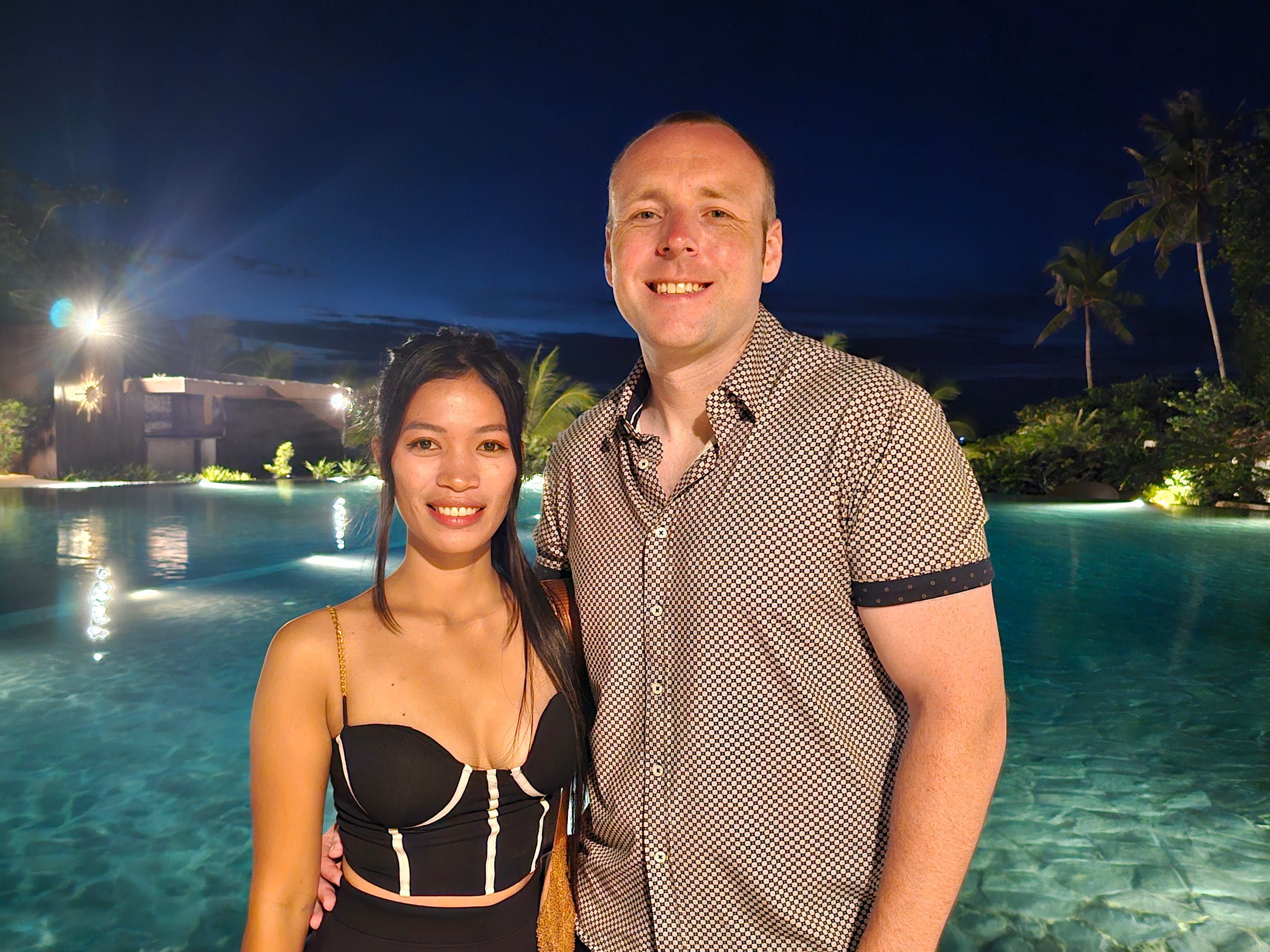 Ein kaukasischer Mann und eine philippinische Frau posieren vor einem Pool.