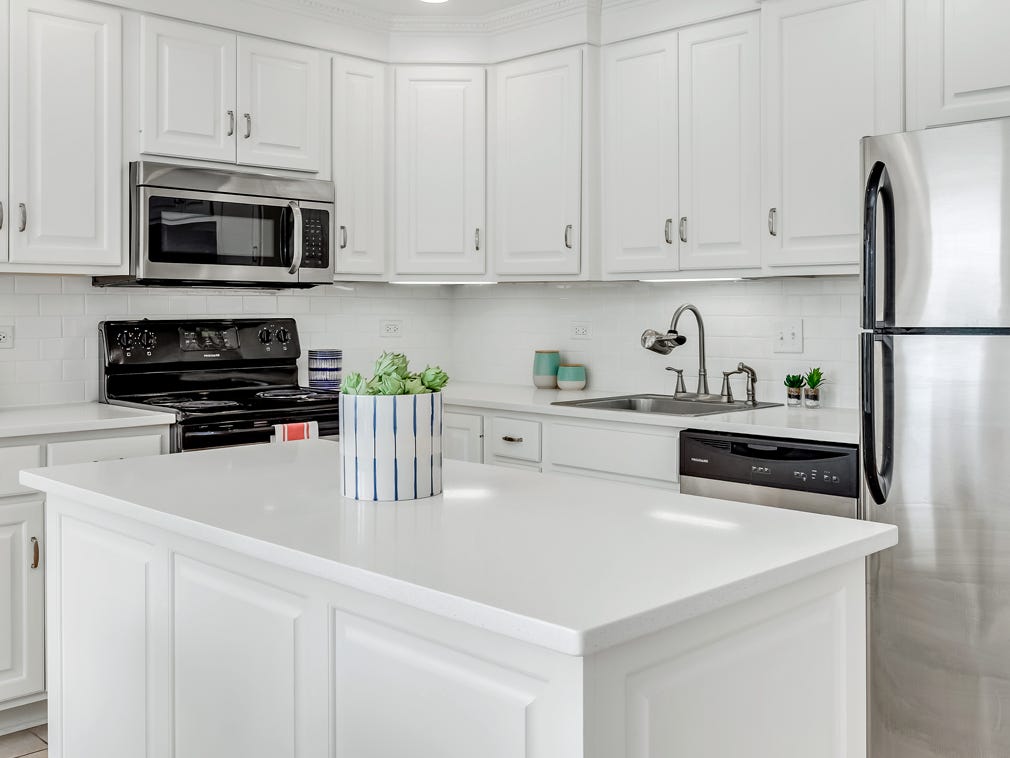 Eine ganz in Weiß gehaltene Küche mit Kühlschrank aus Edelstahl, einem dekorativen Kanister mit Artischocken darin und einem schwarzen Herd