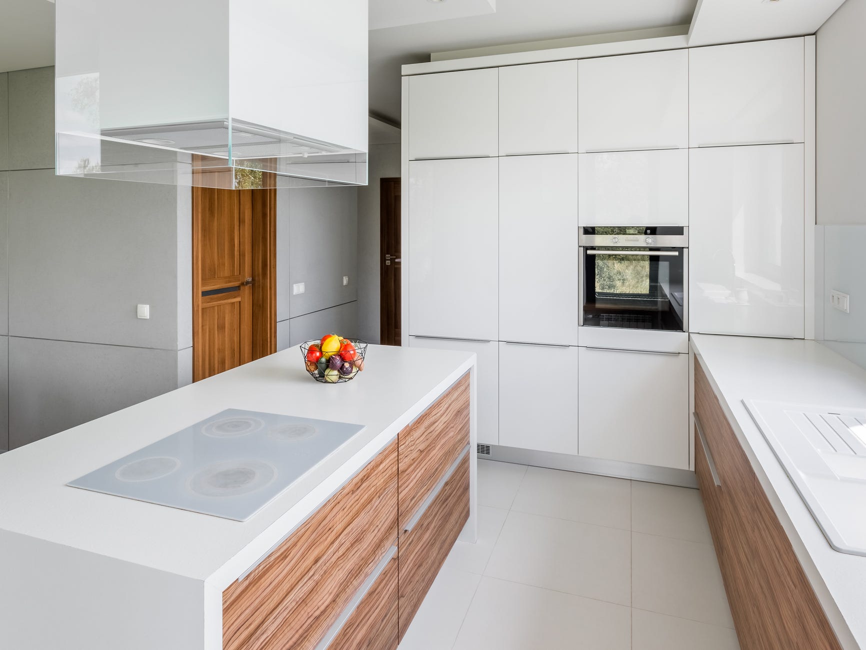 Eine größtenteils weiße Küche mit einigen Holzdetails auf den Arbeitsflächen.  Über einer Kücheninsel hängt eine große rechteckige weiße Leuchte