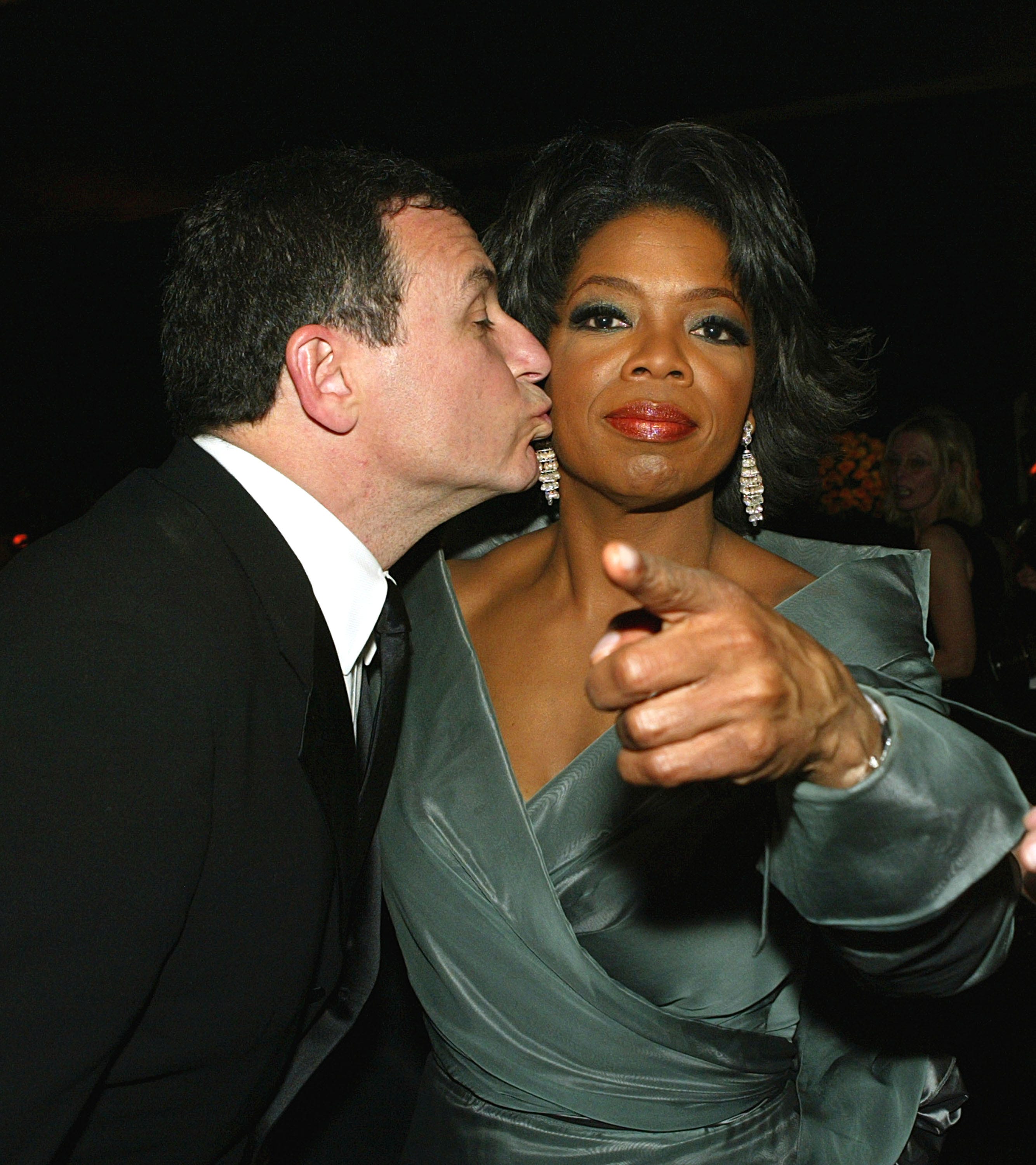 ABC-Präsident Bob Iger (l.) küsst Oprah Winfrey (r.), während sie in die Kamera zeigt.
