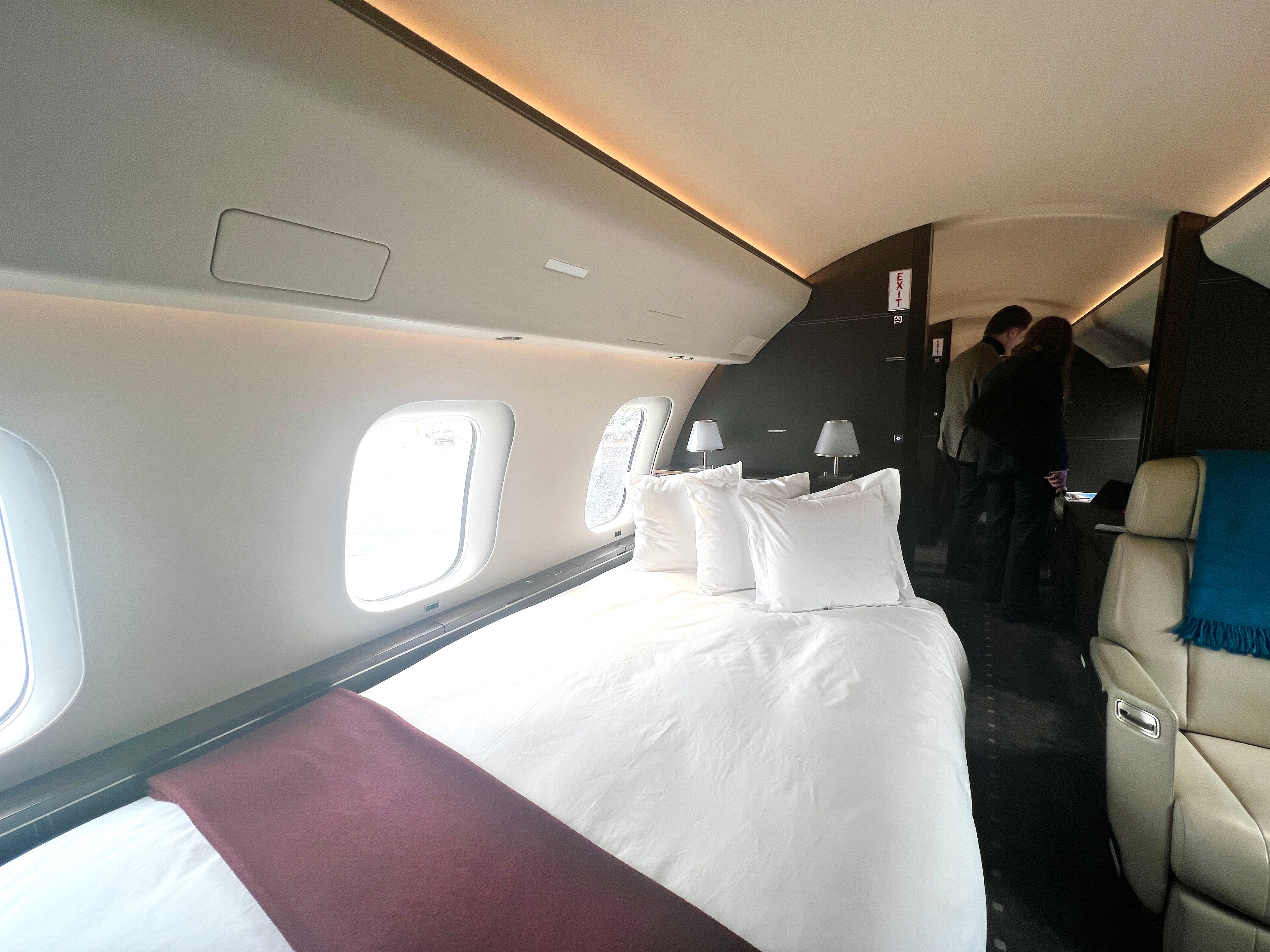 Das Doppelbett an Bord eines VistaJet Bombardier Global 7500 mit weißer Bettwäsche und einer kastanienbraunen Decke.