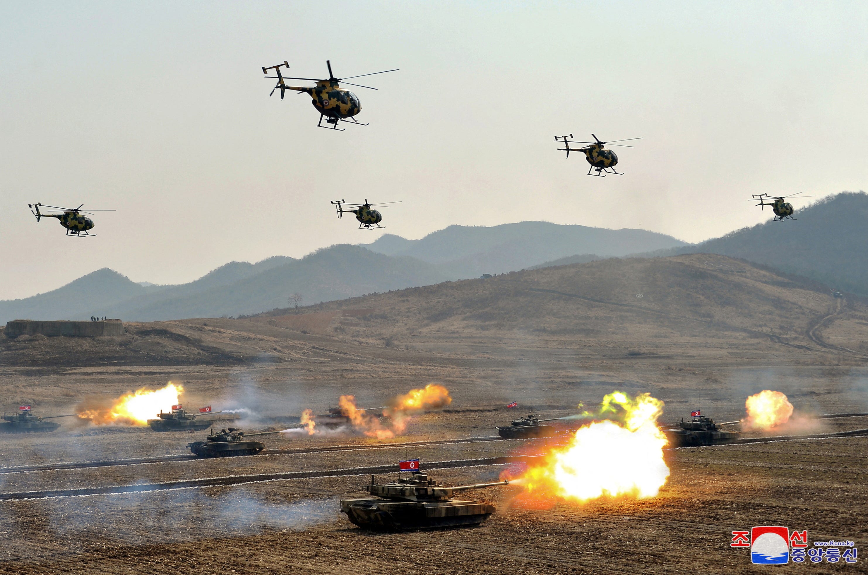 Während einer Militärdemonstration in Nordkorea fliegen Militärhubschrauber über schießenden Panzern.