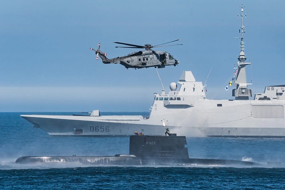 Im Hintergrund ist die Fregatte FNS Alsace der französischen Marine zu sehen, während ein CH-148 Cyclone Maritime Helicopter eine Hebeübung durchführt