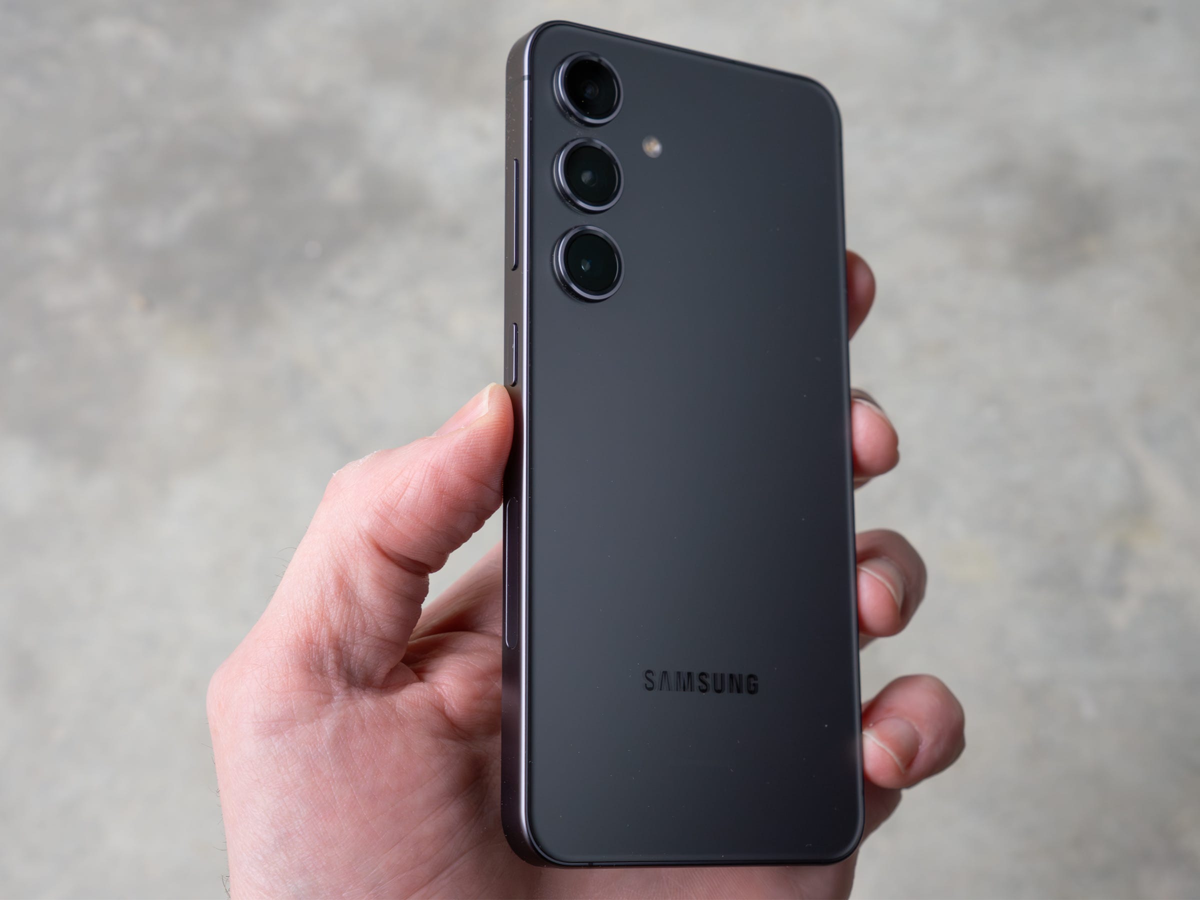 Das Samsung Galaxy S24 wird leicht schräg in der Hand gehalten und zeigt die Seite und die Rückseite.