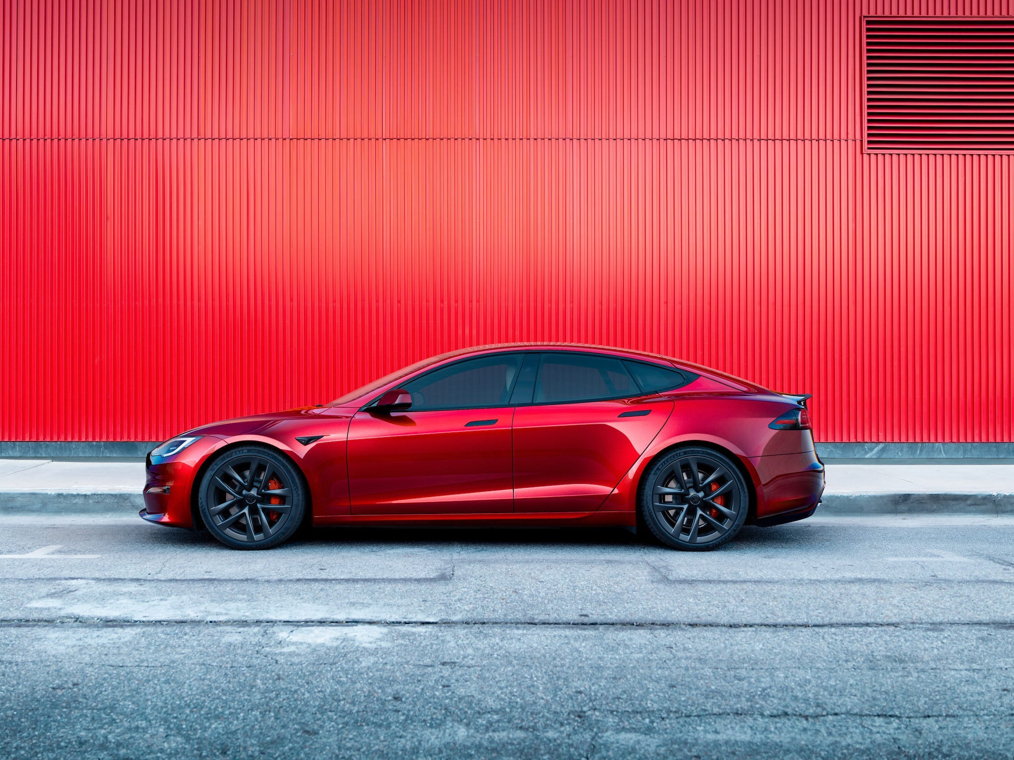 Ein roter Tesla Model S parkte auf einer gepflasterten Straße vor einem roten Gebäude.
